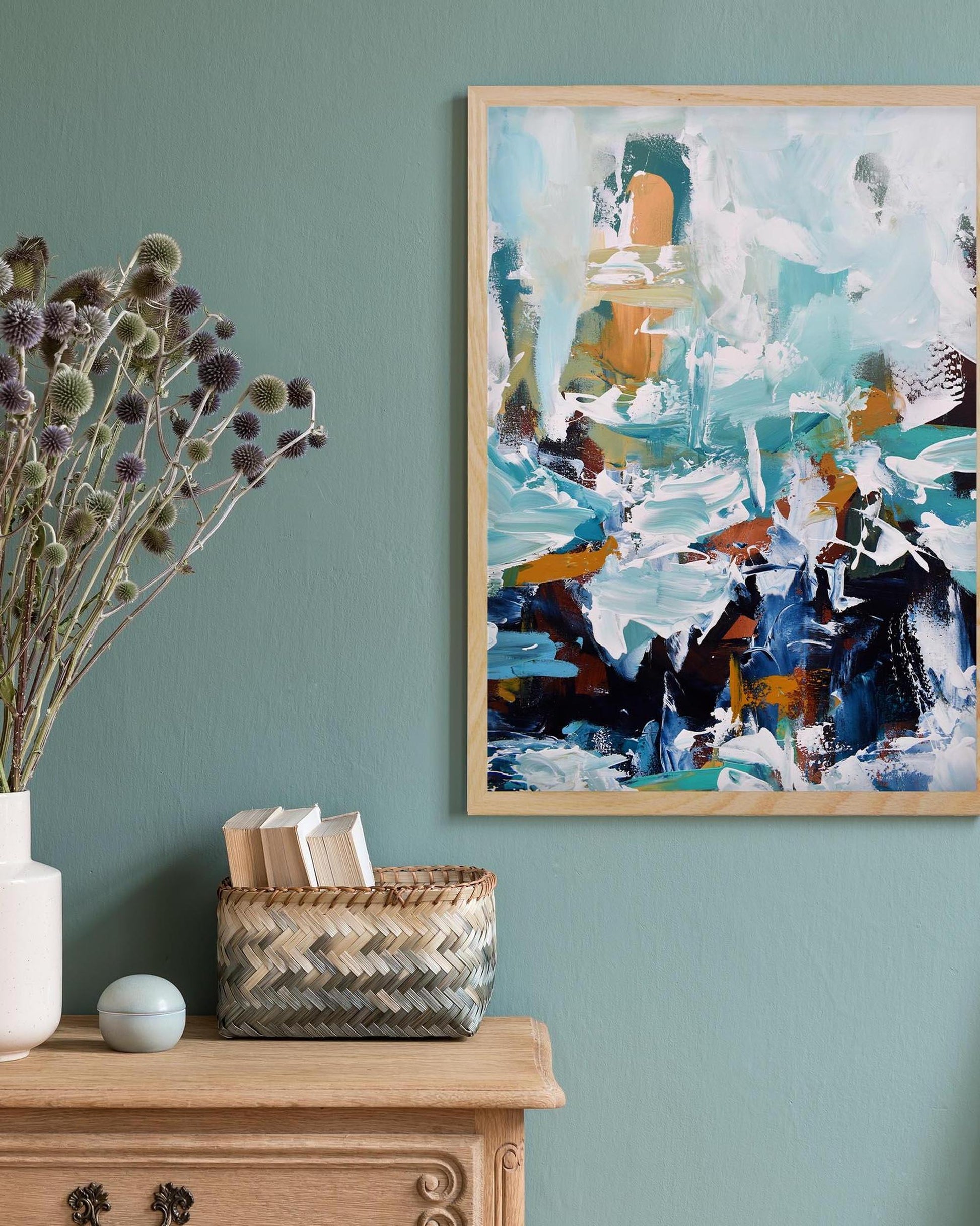 Abstract painting on a teal wall with a wooden cabinet and decorative items.