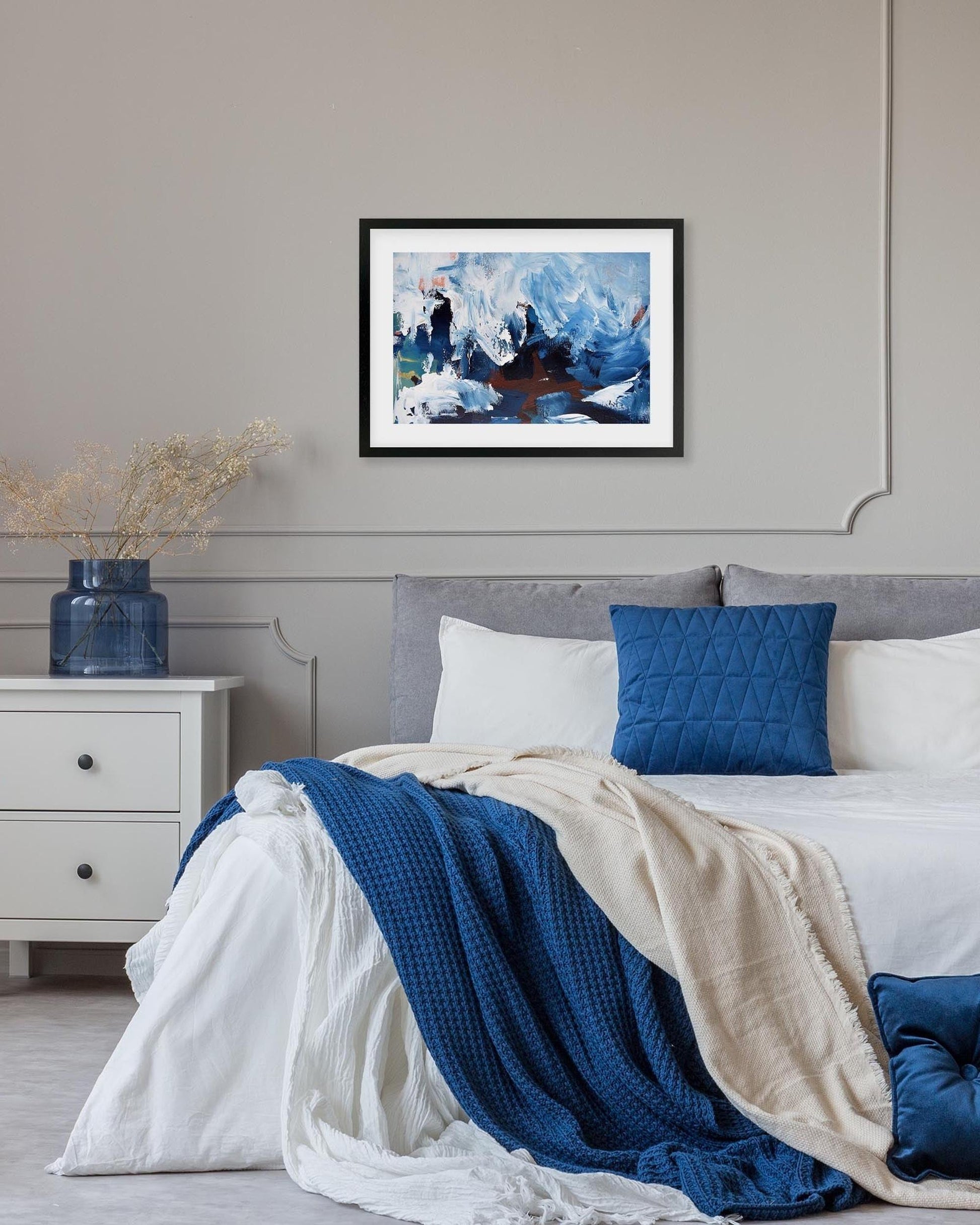 Bedroom with a bed featuring blue and white bedding, a nightstand, and a framed abstract painting on the wall.