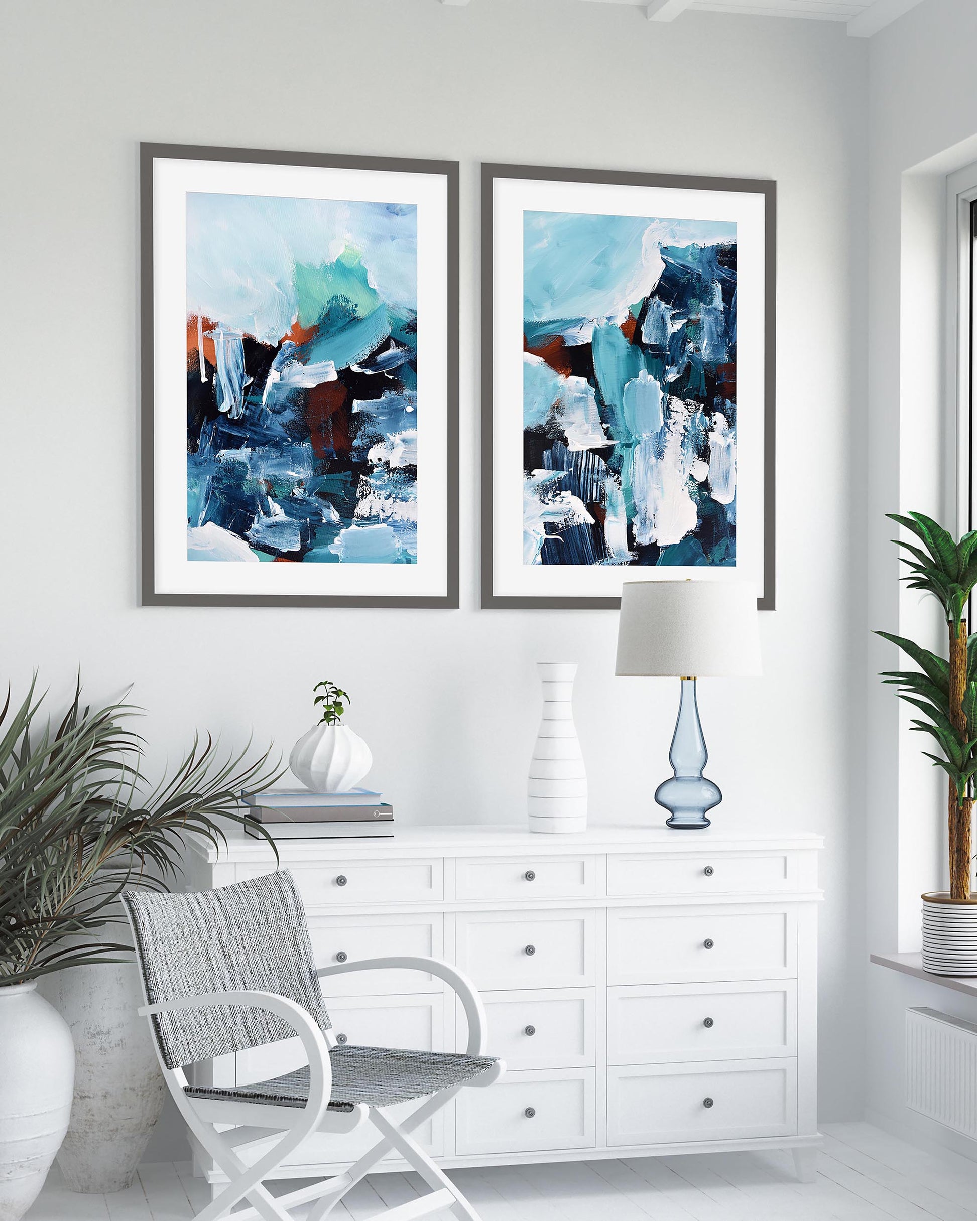 A set of two framed abstract art prints featuring blue tones, displayed on a wall above a white dresser in a bright room.