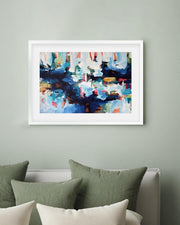 Framed abstract painting on a wall above a bed with green and white pillows.