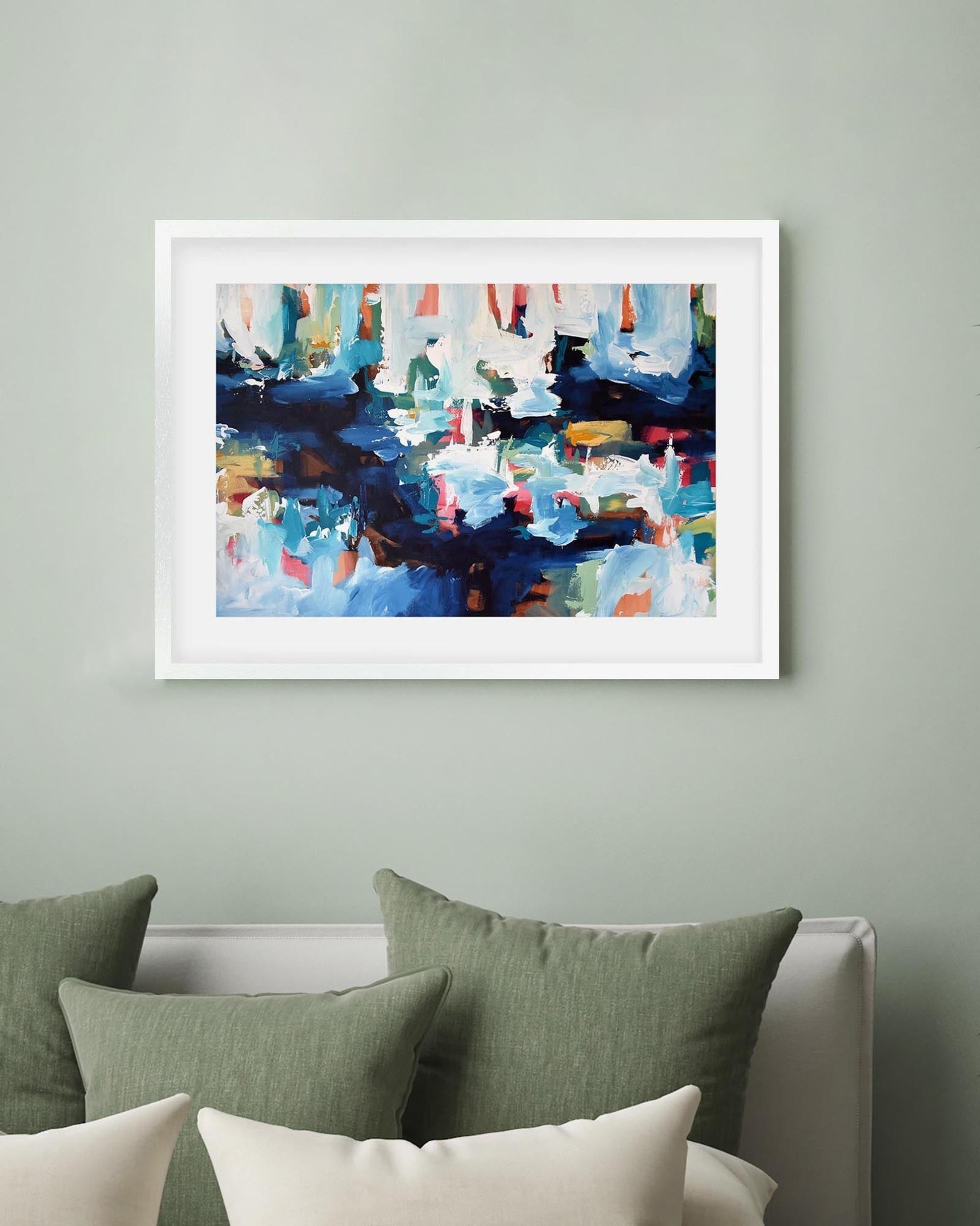 Framed abstract painting on a wall above a bed with green and white pillows.