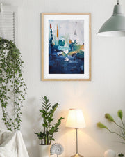 Framed abstract art piece on a wall with plants and a lamp in the room.