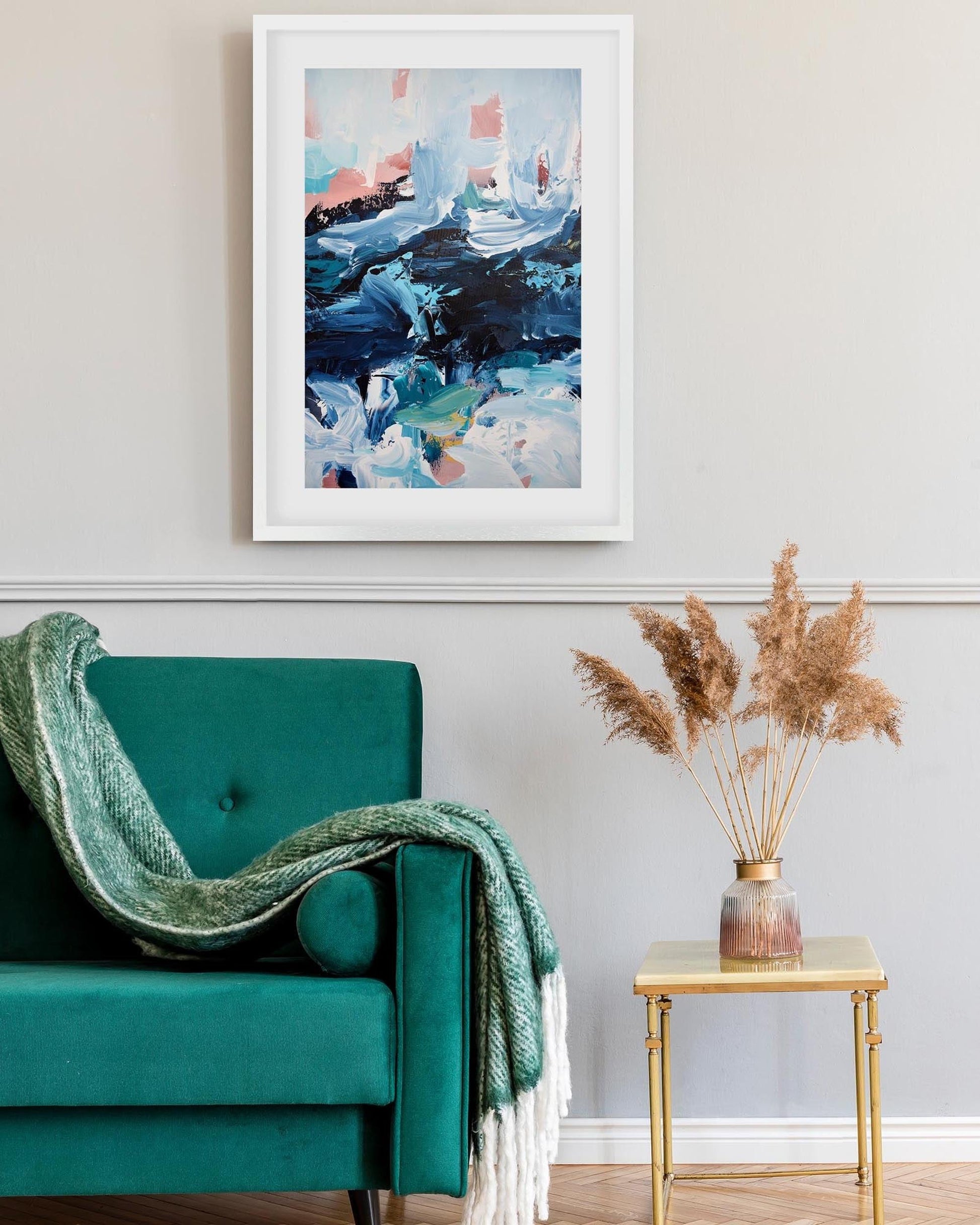 Teal sofa with a green blanket, gold side table with dried plants, and abstract art on the wall.