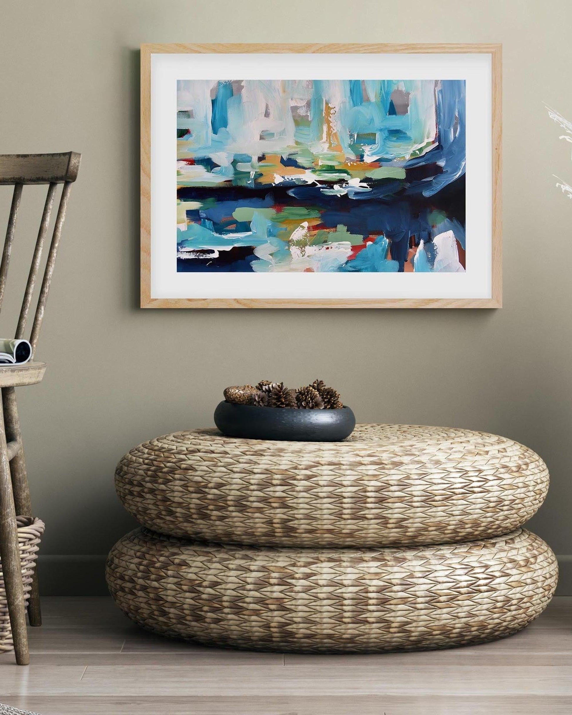 Abstract painting on a wall above a woven ottoman with decorative elements.