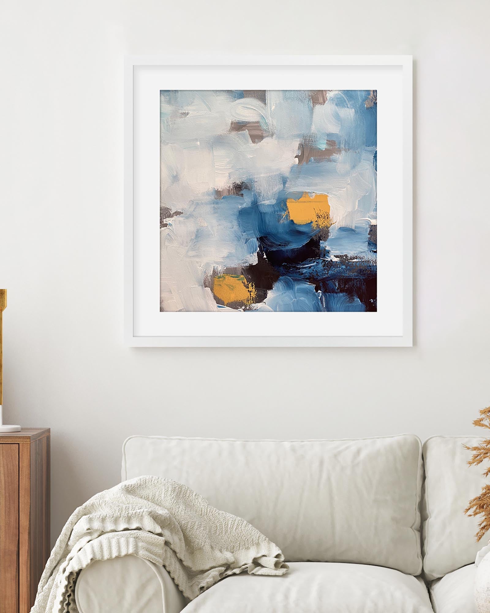 Abstract art print in a white frame on a wall above a sofa.
