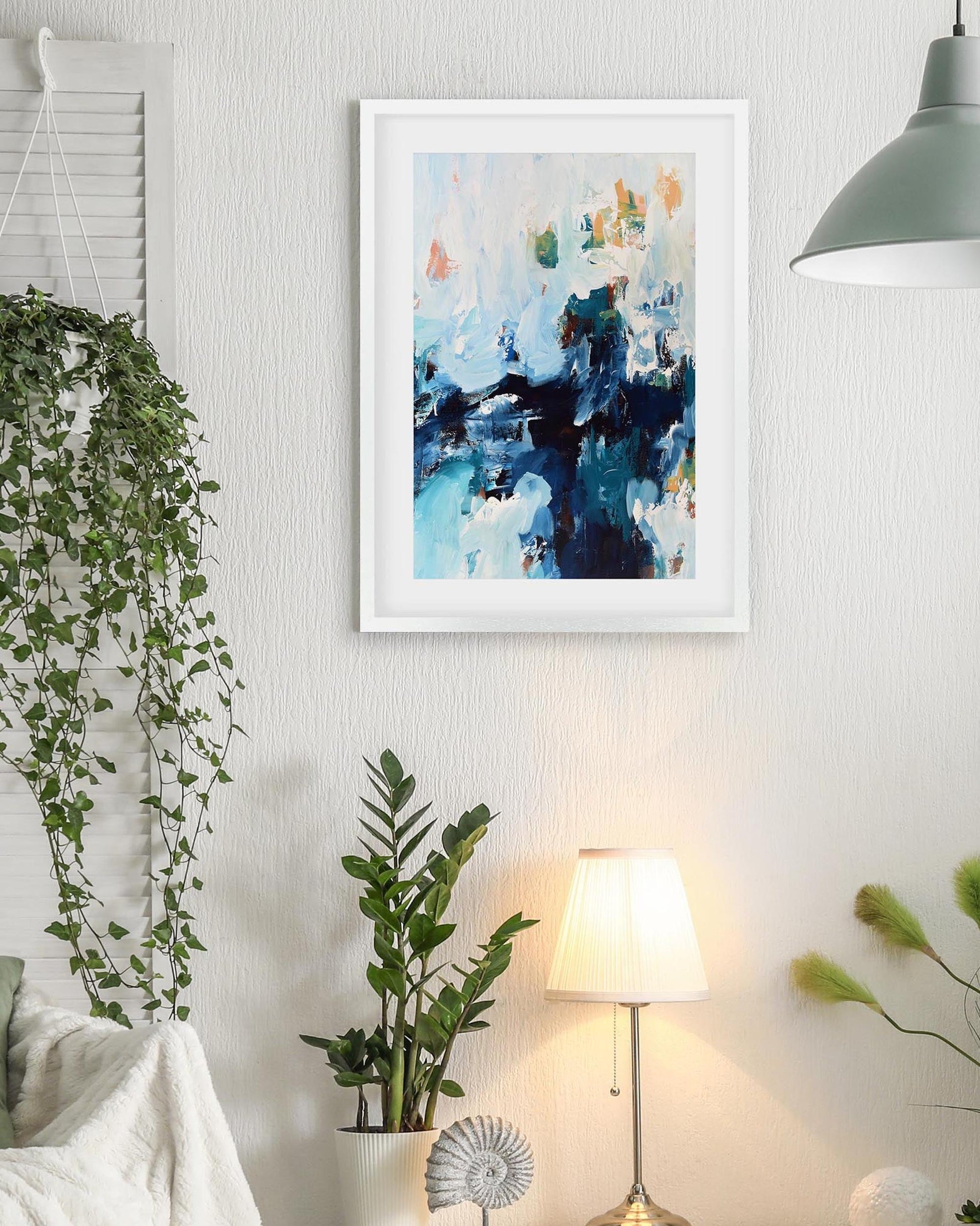 Living room with plants, a lamp, and a framed abstract painting on the wall.