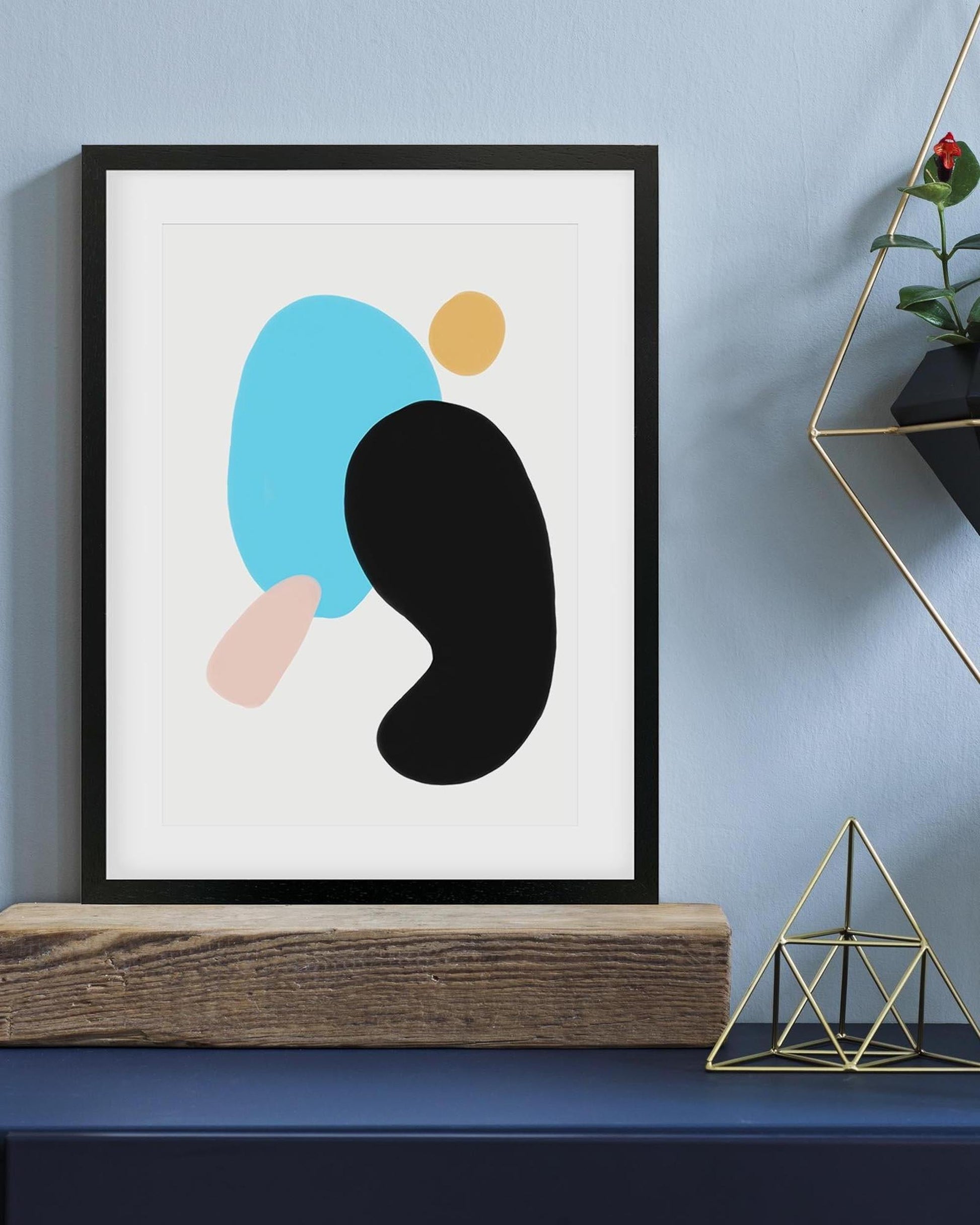 Framed abstract art print with colorful shapes on a blue wall.