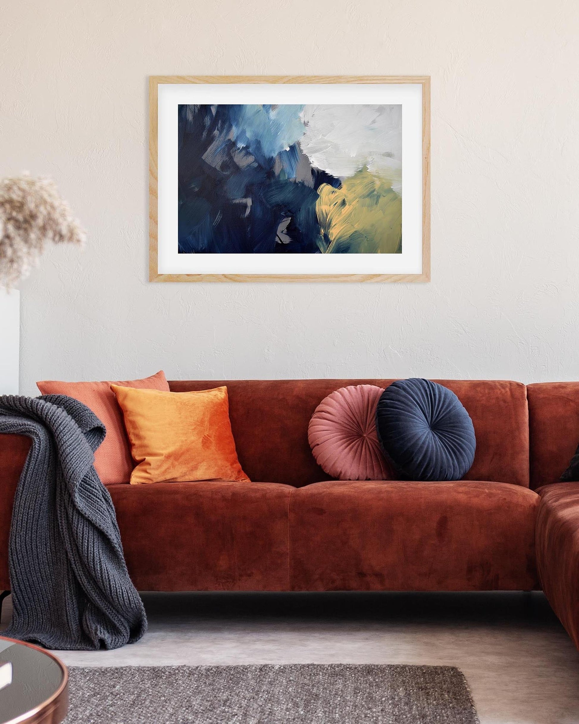 Living room with a brown sofa, colorful cushions, and a framed abstract painting on the wall.