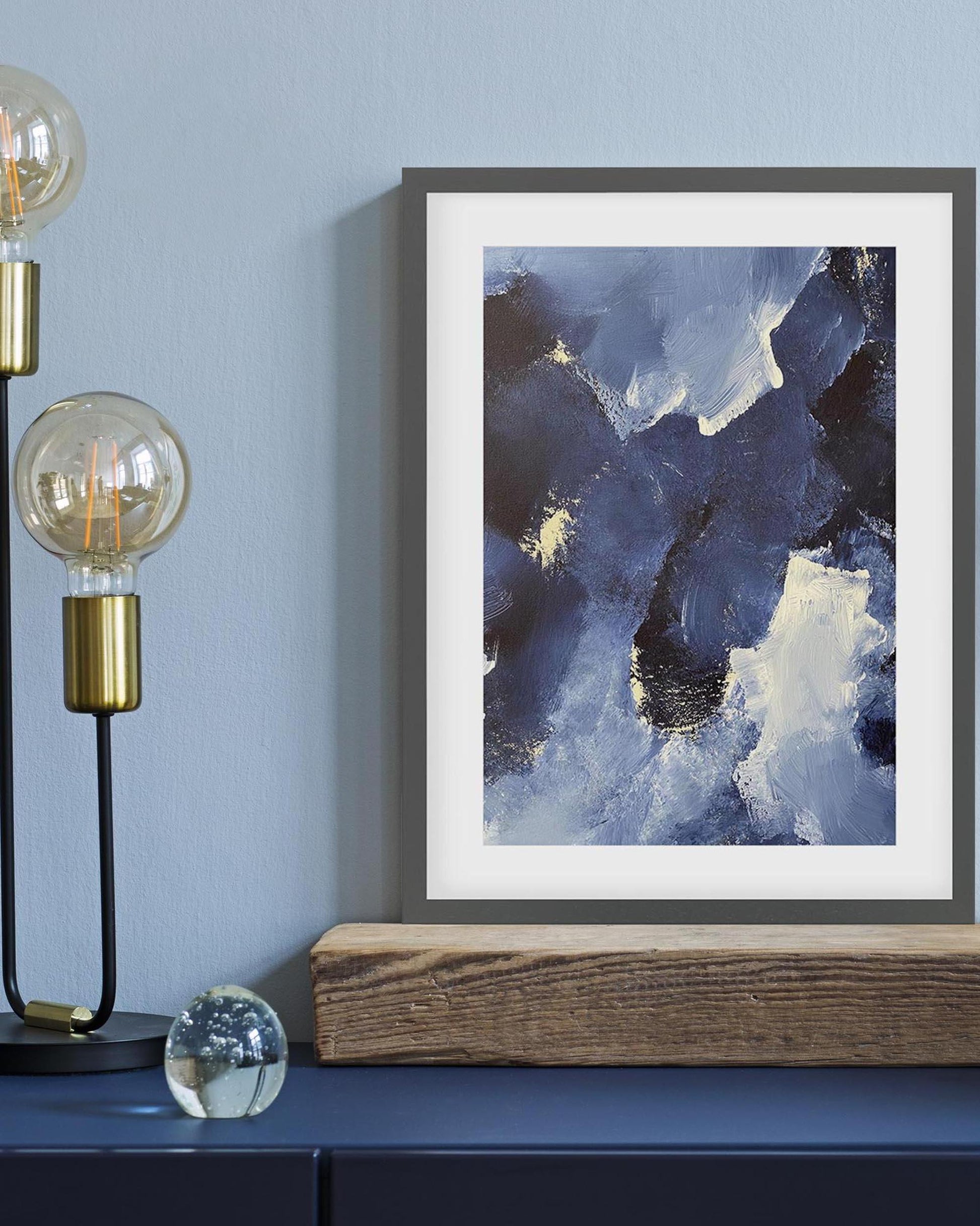 Framed abstract art piece on a wall with a lamp and decorative elements below.