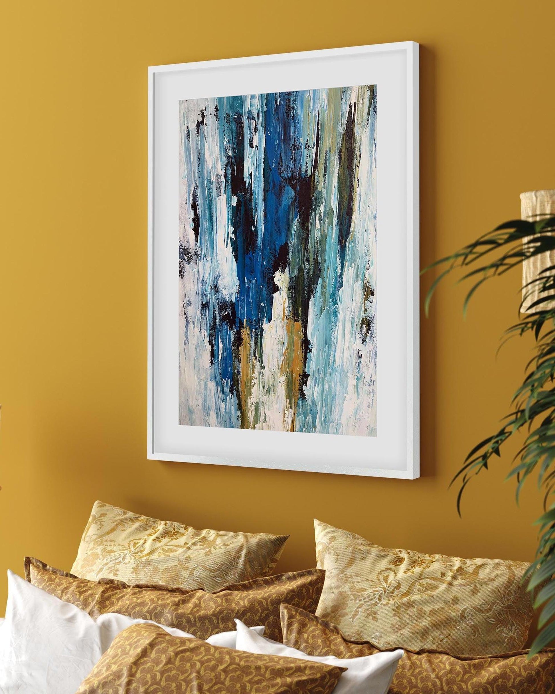 Framed abstract art on a mustard yellow wall with pillows and a plant.