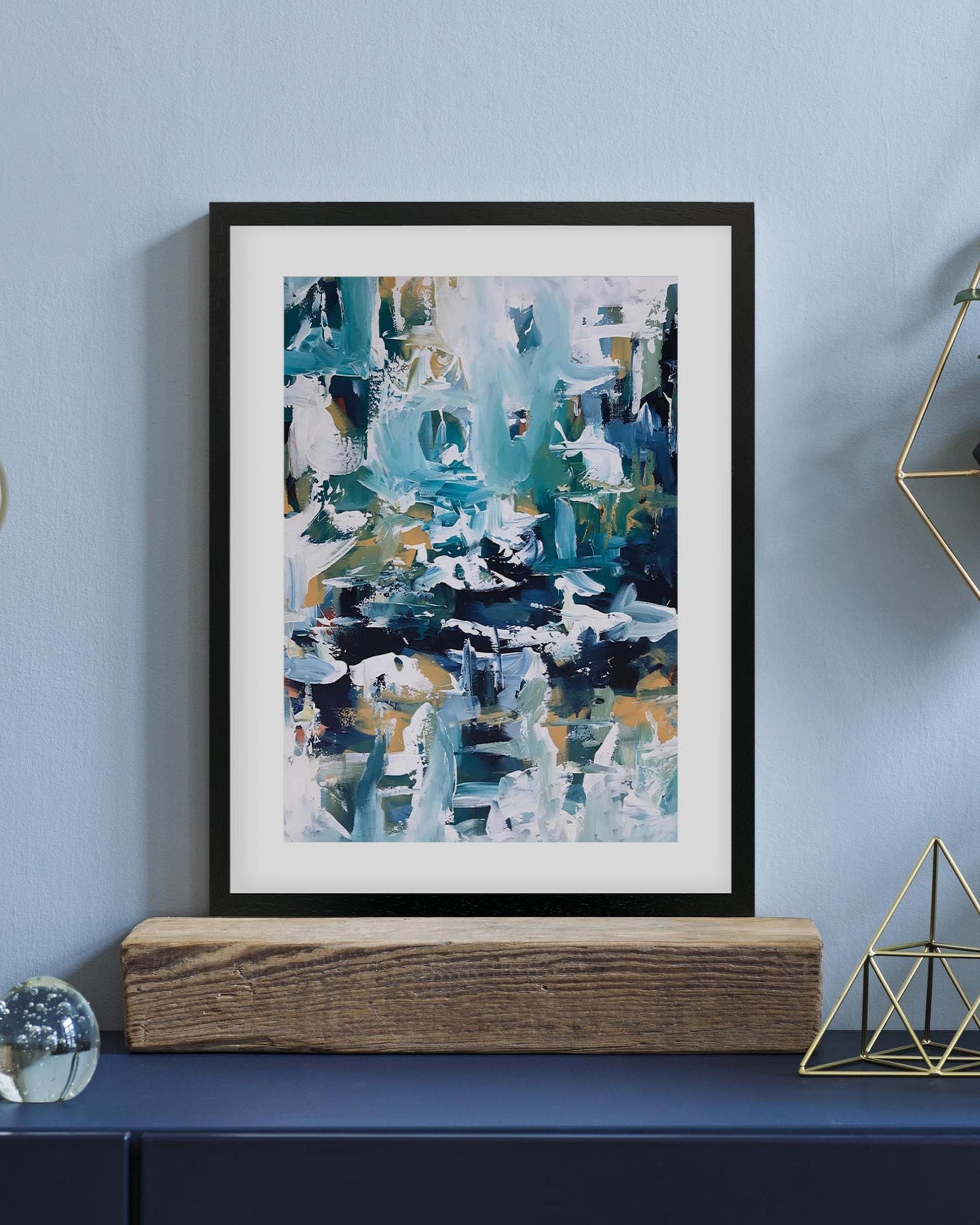 Framed abstract art piece on a shelf with decorative items against a light blue wall.