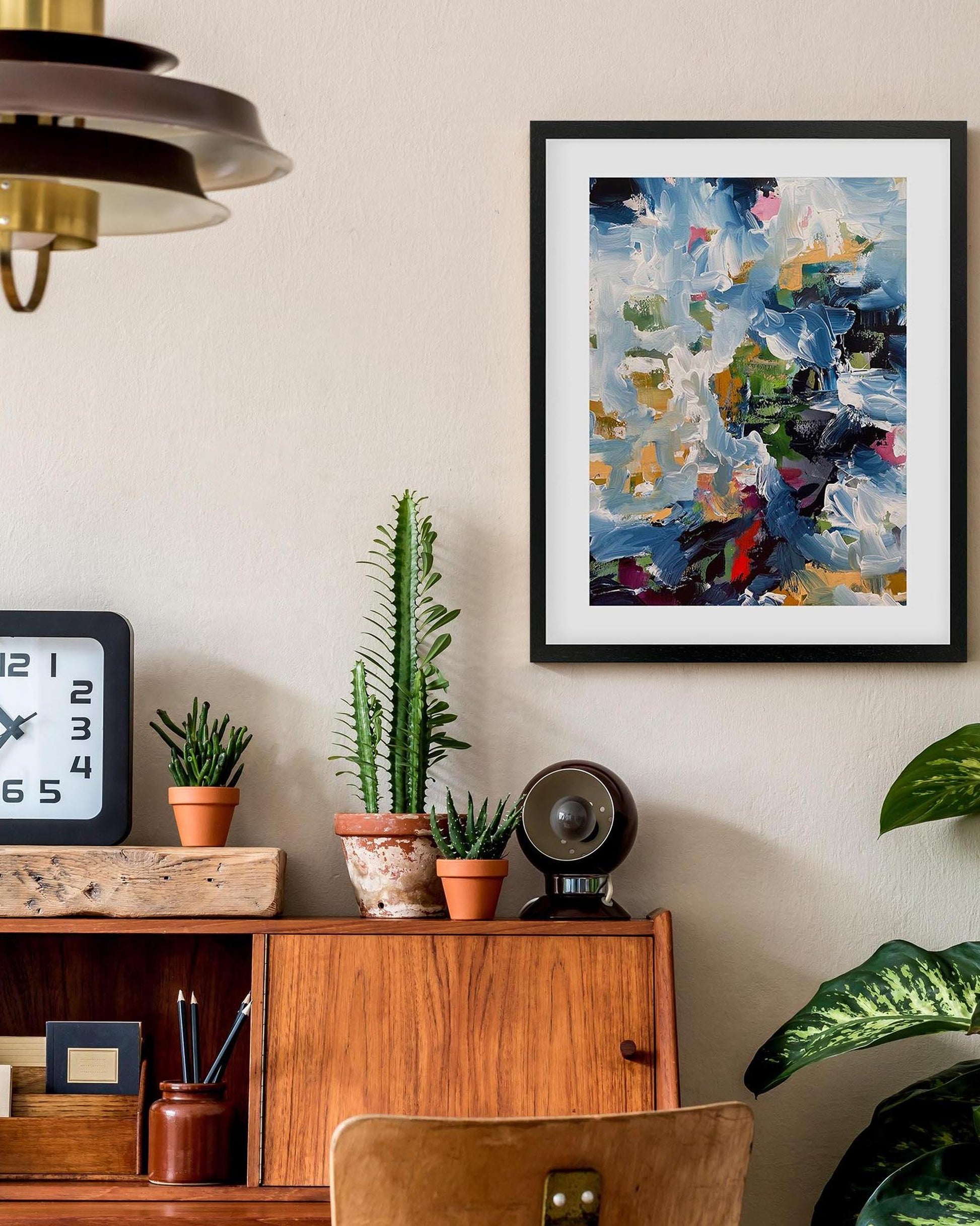 Framed abstract painting on a wall above a wooden cabinet with decorative items.