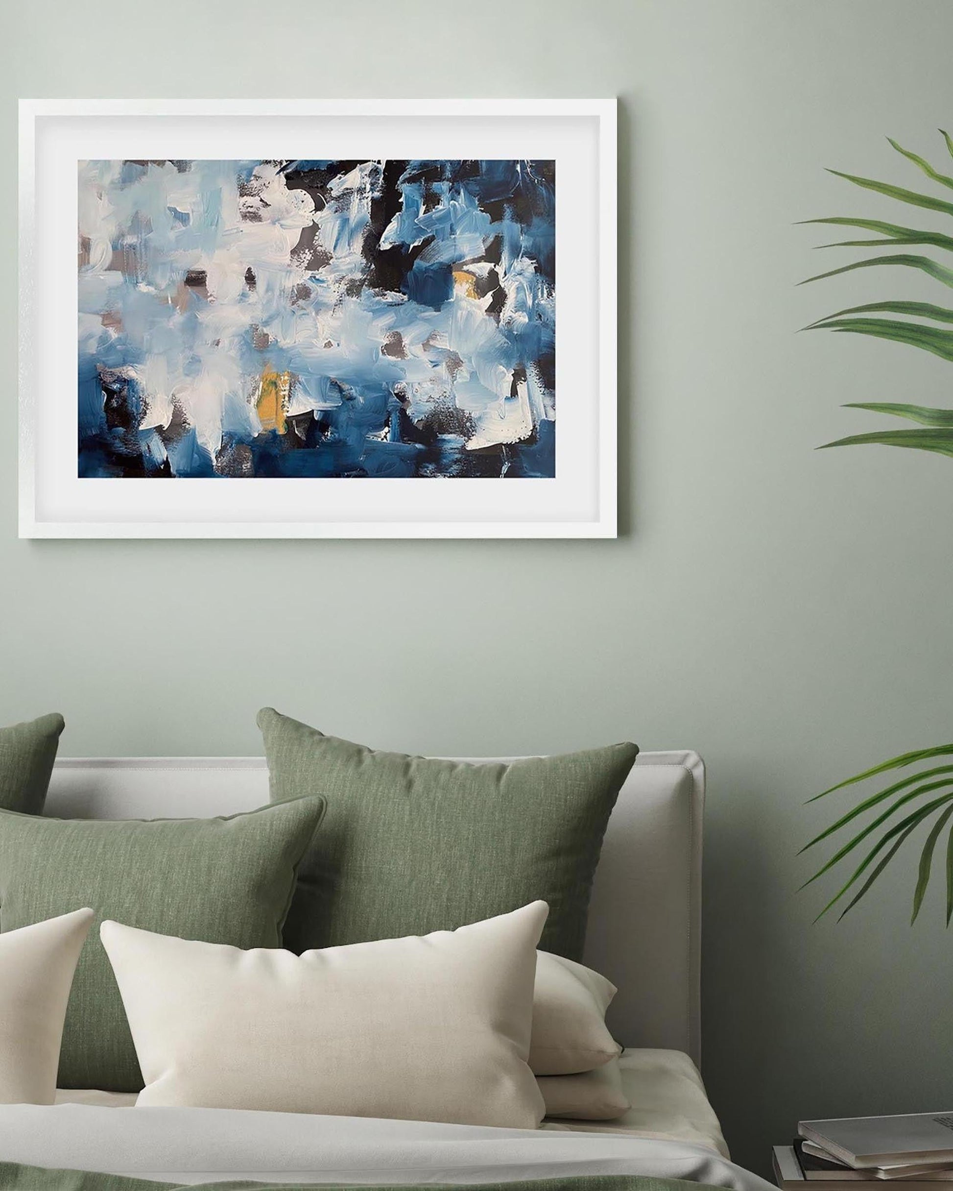 Framed abstract painting on a wall above a sofa with green and white cushions.
