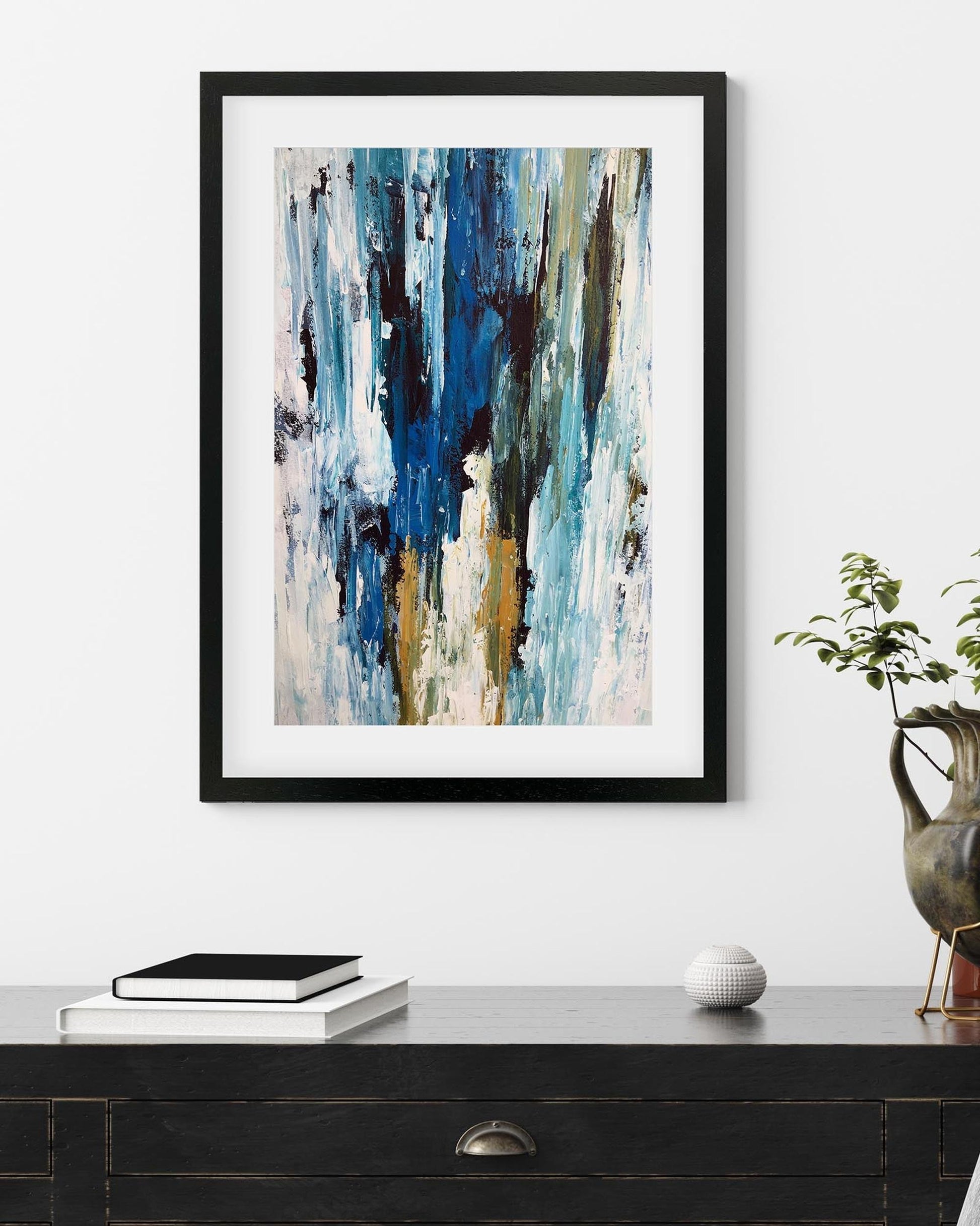 Framed abstract art piece on a wall above a desk with decorative items.