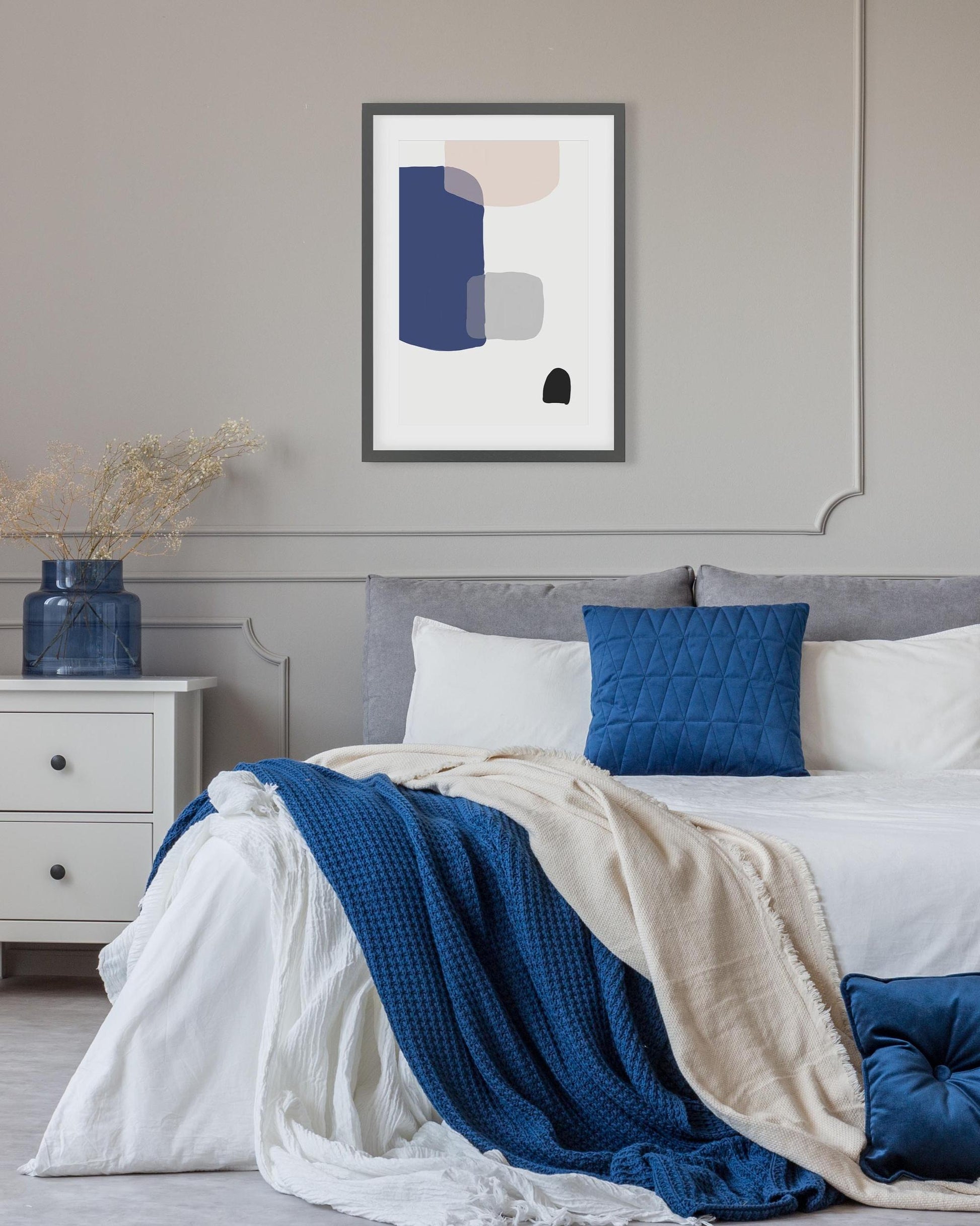 Bedroom with abstract art on the wall, blue and beige bedding, and a nightstand.