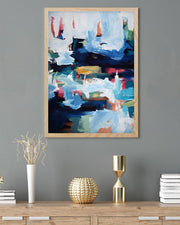 Abstract painting in a wooden frame on a gray wall above a wooden console table with decorative items.