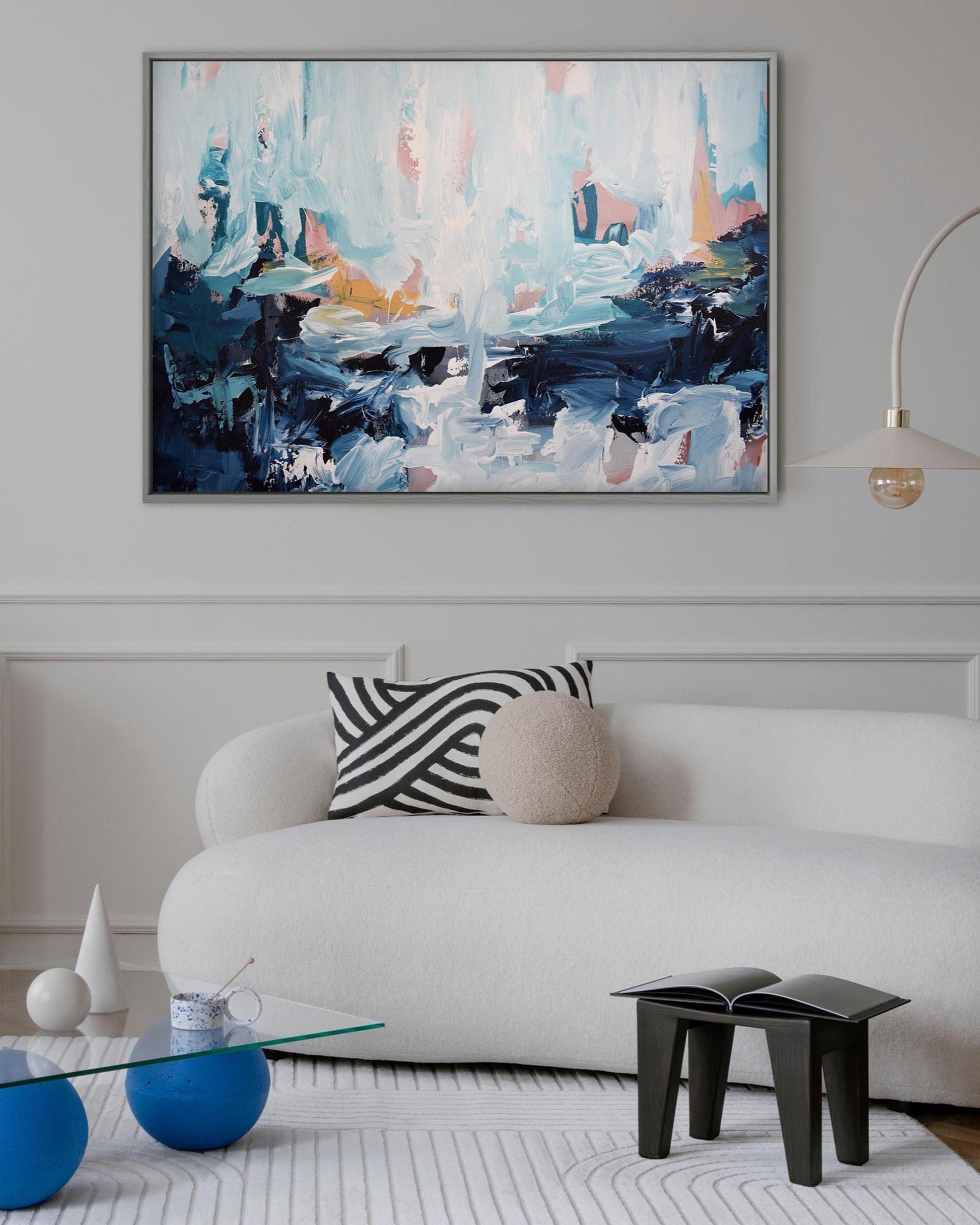 Modern living room with a white sofa, abstract painting, and decorative items.