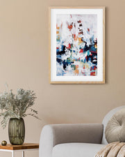 Abstract art print in a wooden frame on a beige wall above a sofa.
