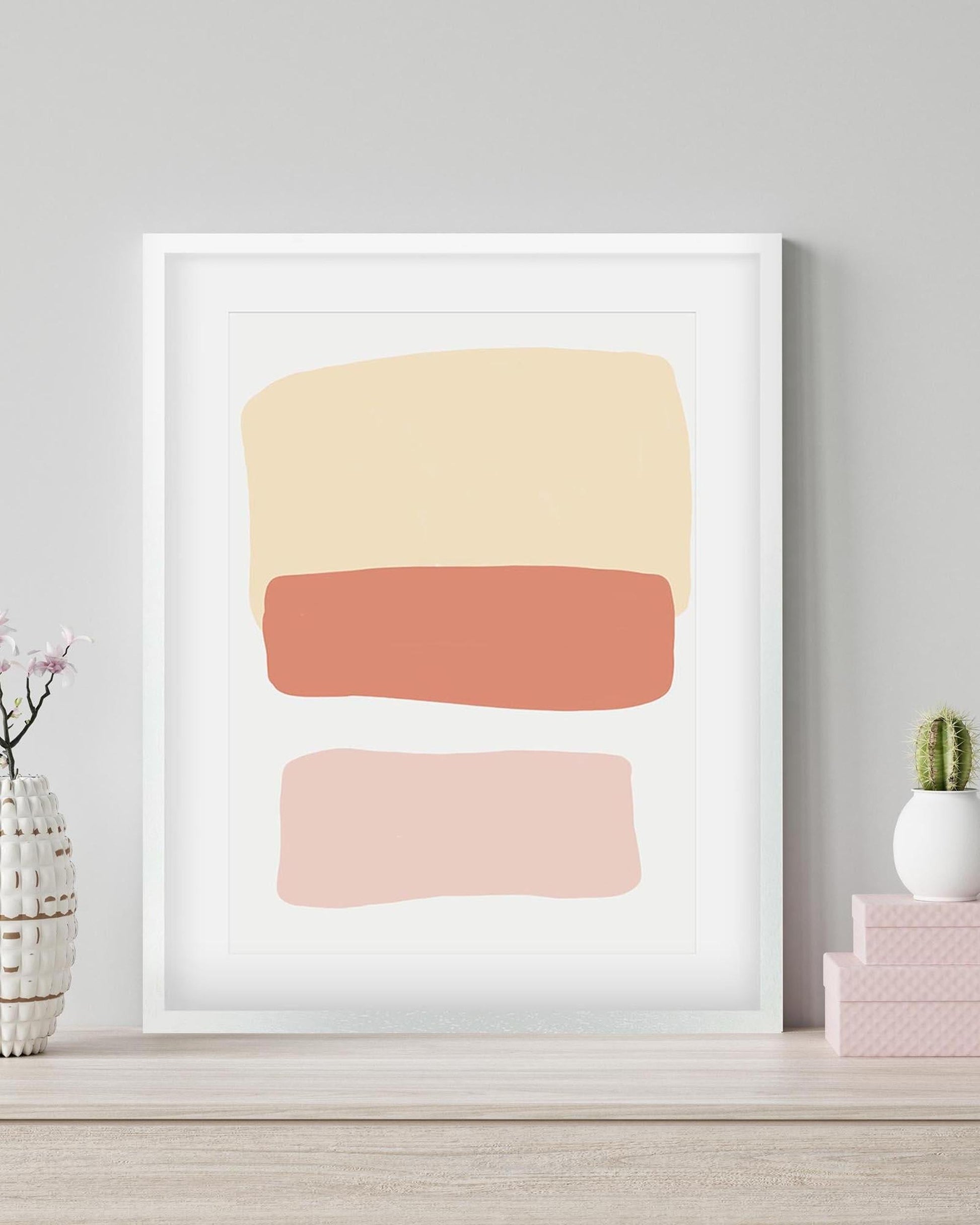 Framed abstract art print with three colored shapes on a light gray wall.
