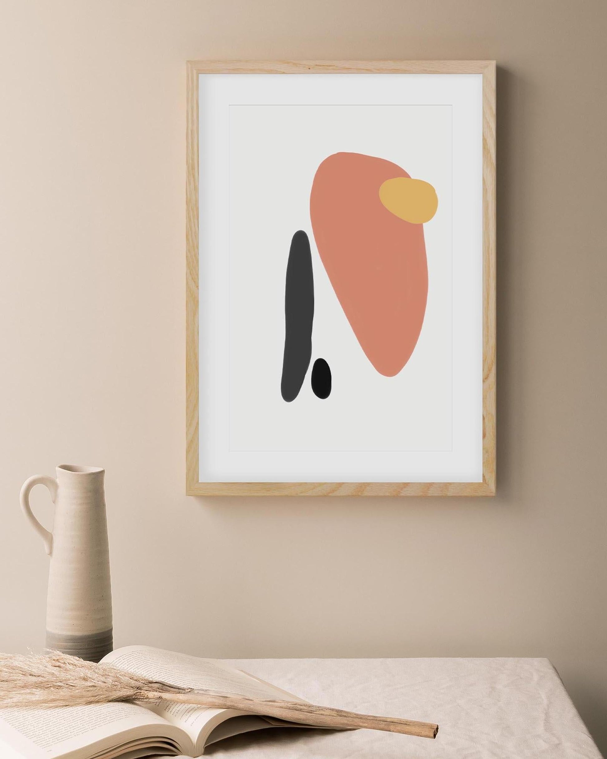 Framed abstract art print on a wall with a vase and book in the foreground.