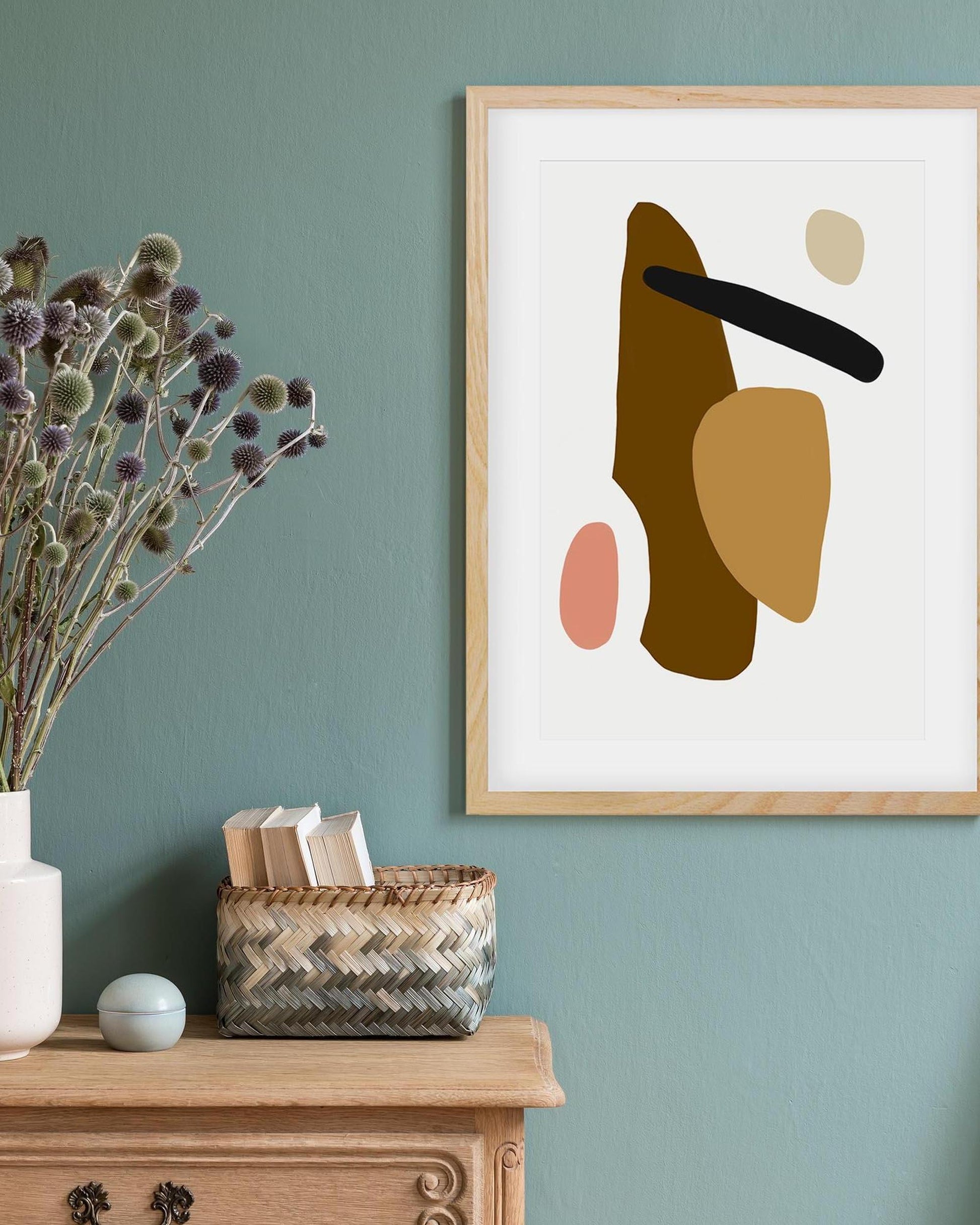Abstract art print on a wall with a vase, books, and basket on a wooden surface below.