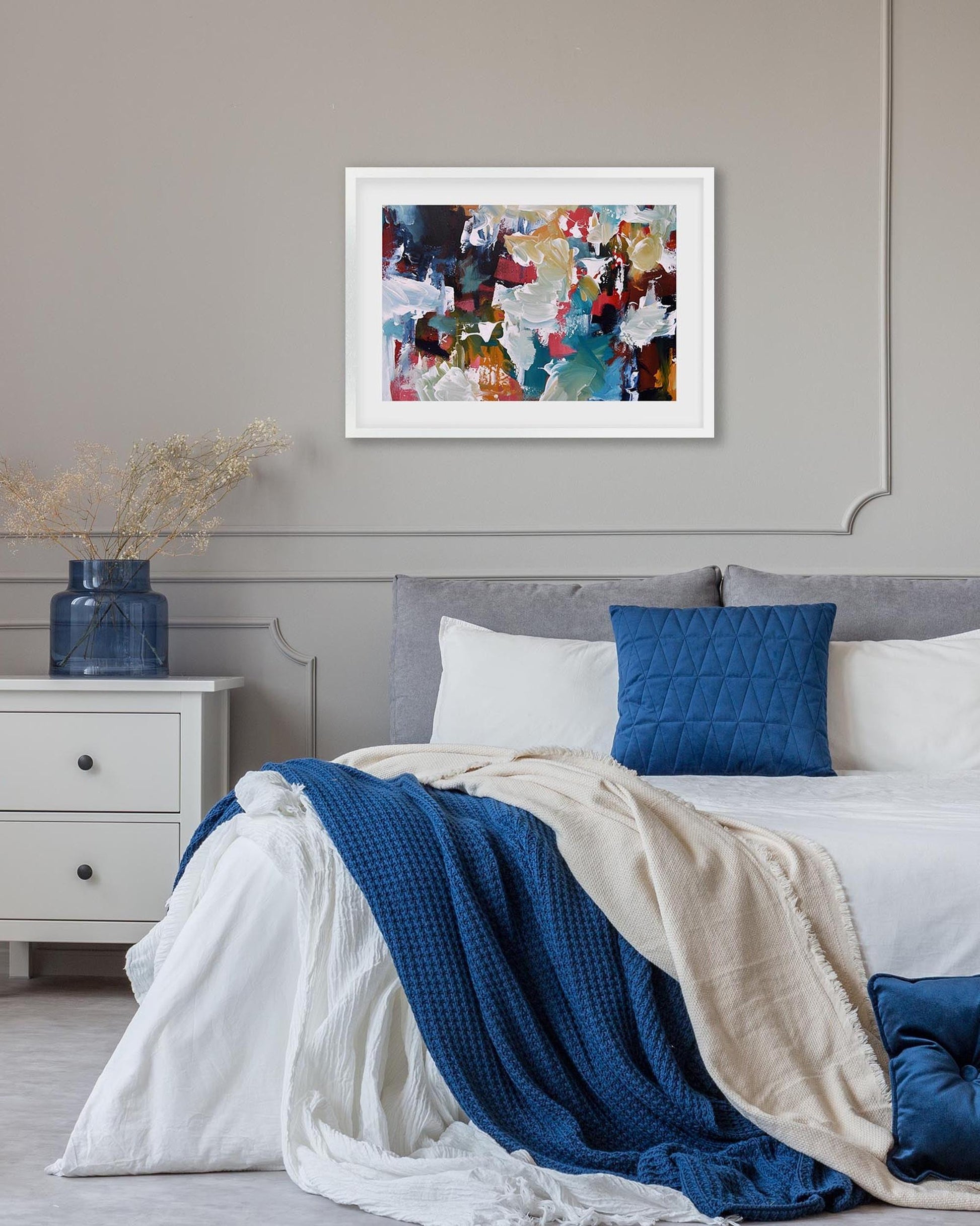 Bedroom with a bed featuring blue and white bedding, a nightstand with a blue vase, and abstract art on the wall.