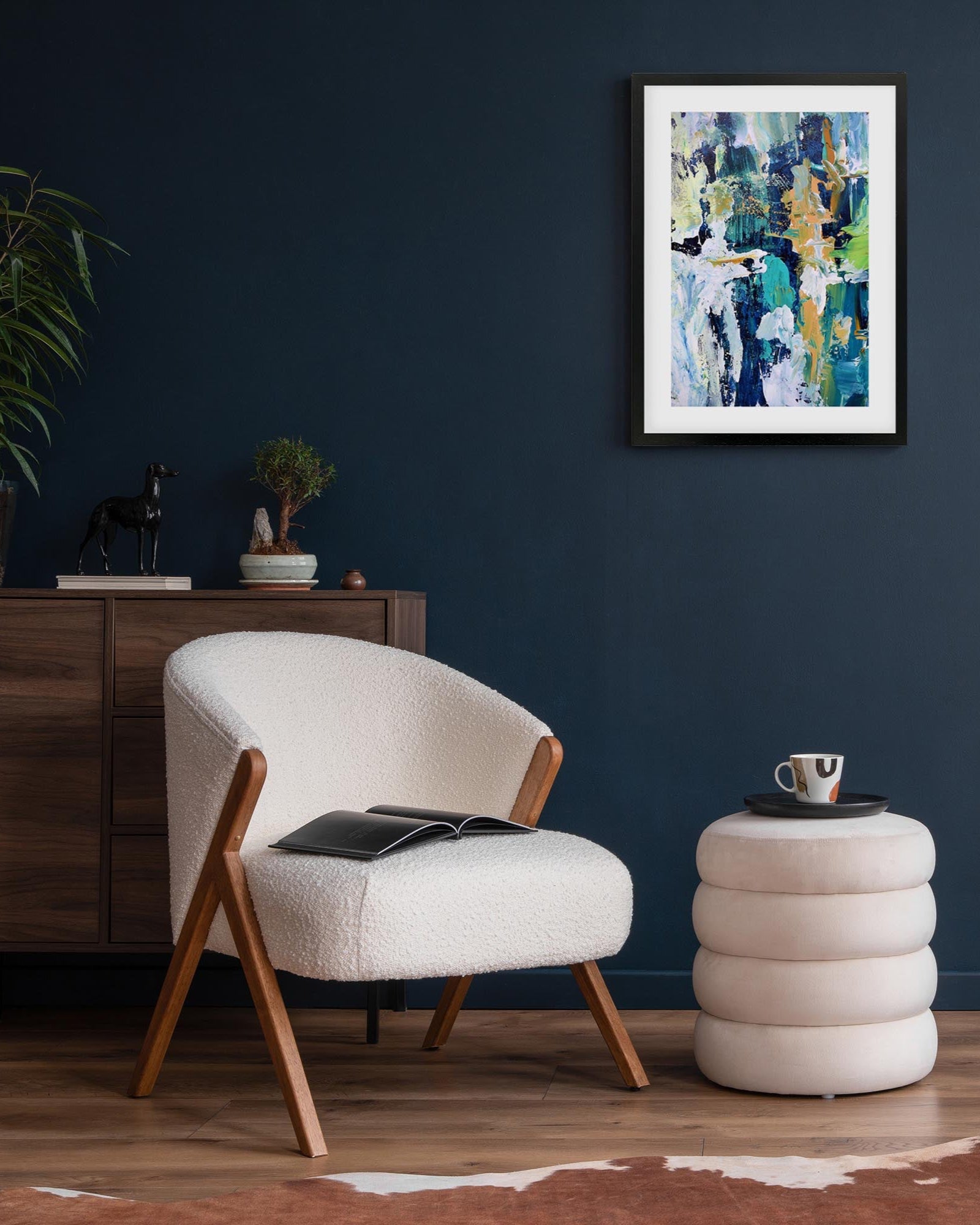 Modern living room with a white armchair, round ottoman, and abstract art on the wall.