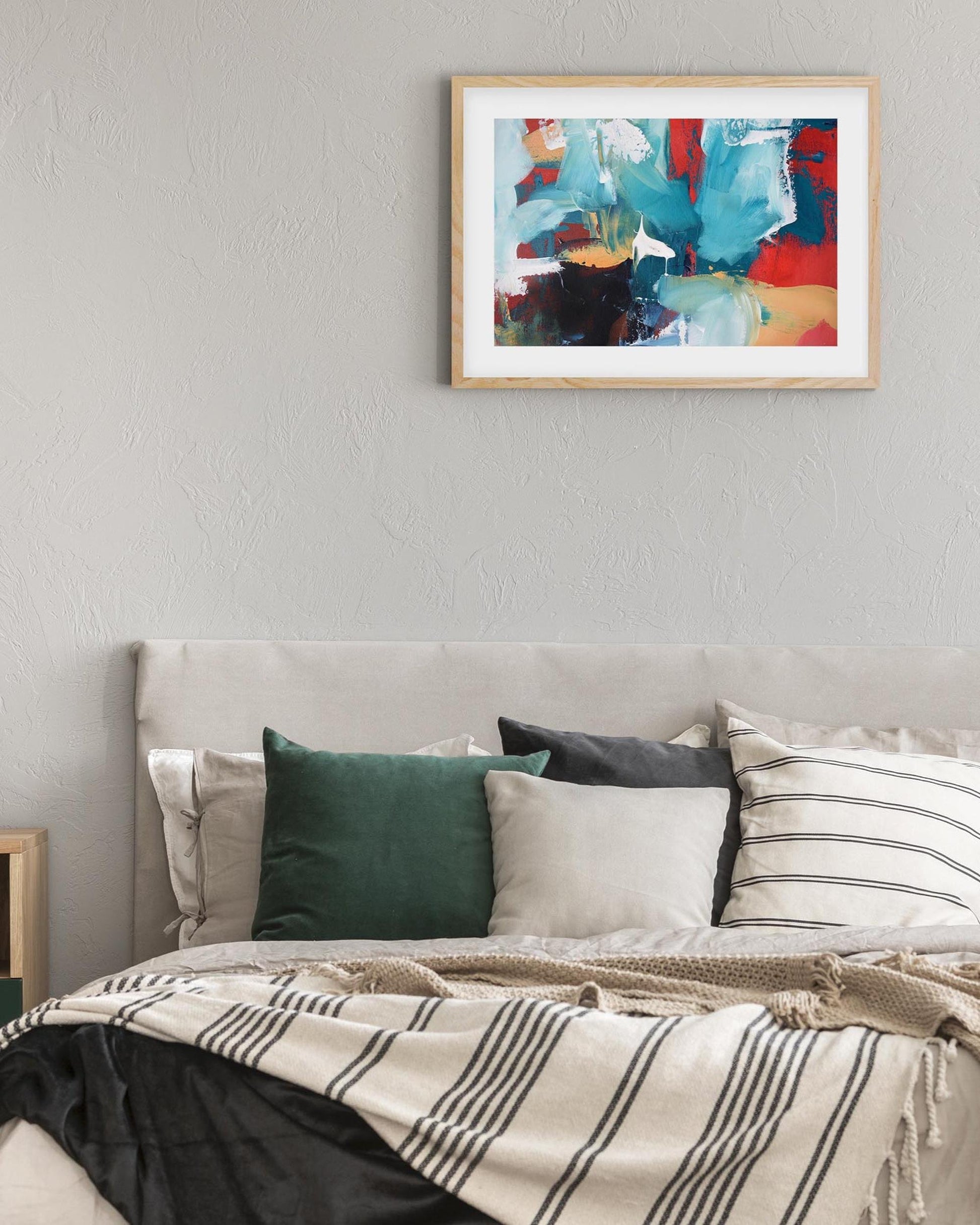 framed abstract art print in oak frame on a wall above a bed