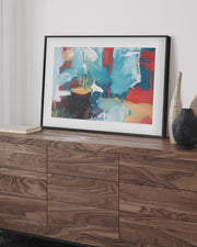 framed abstract art print in a black frame on a wooden sideboard