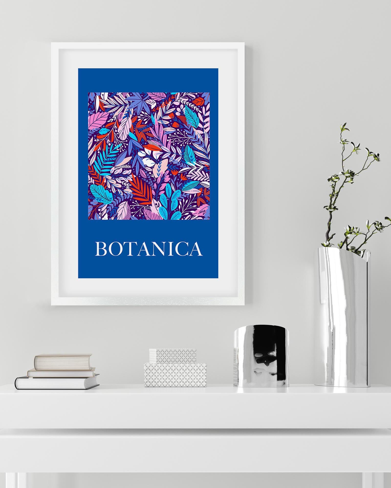 Framed artwork with 'BOTANICA' text and colorful leaf pattern on a blue background, displayed on a shelf.