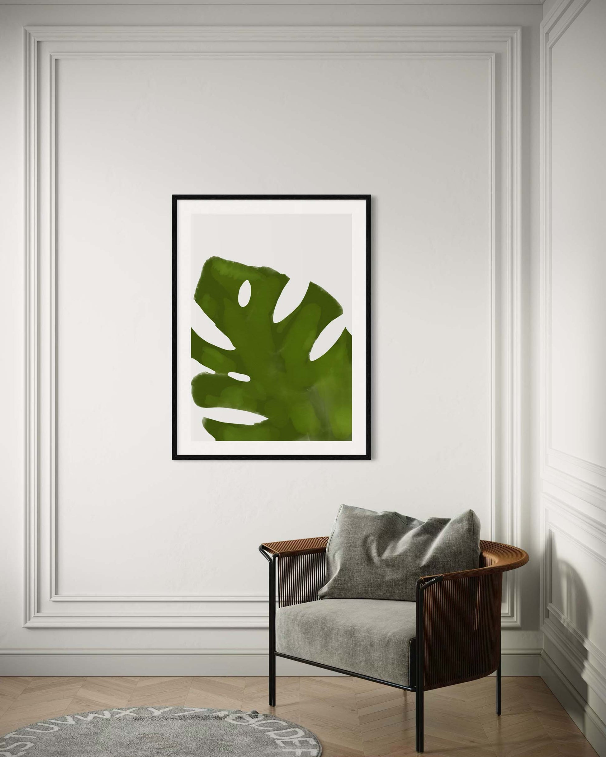 Framed green leaf art print on a wall above a chair with a gray cushion.