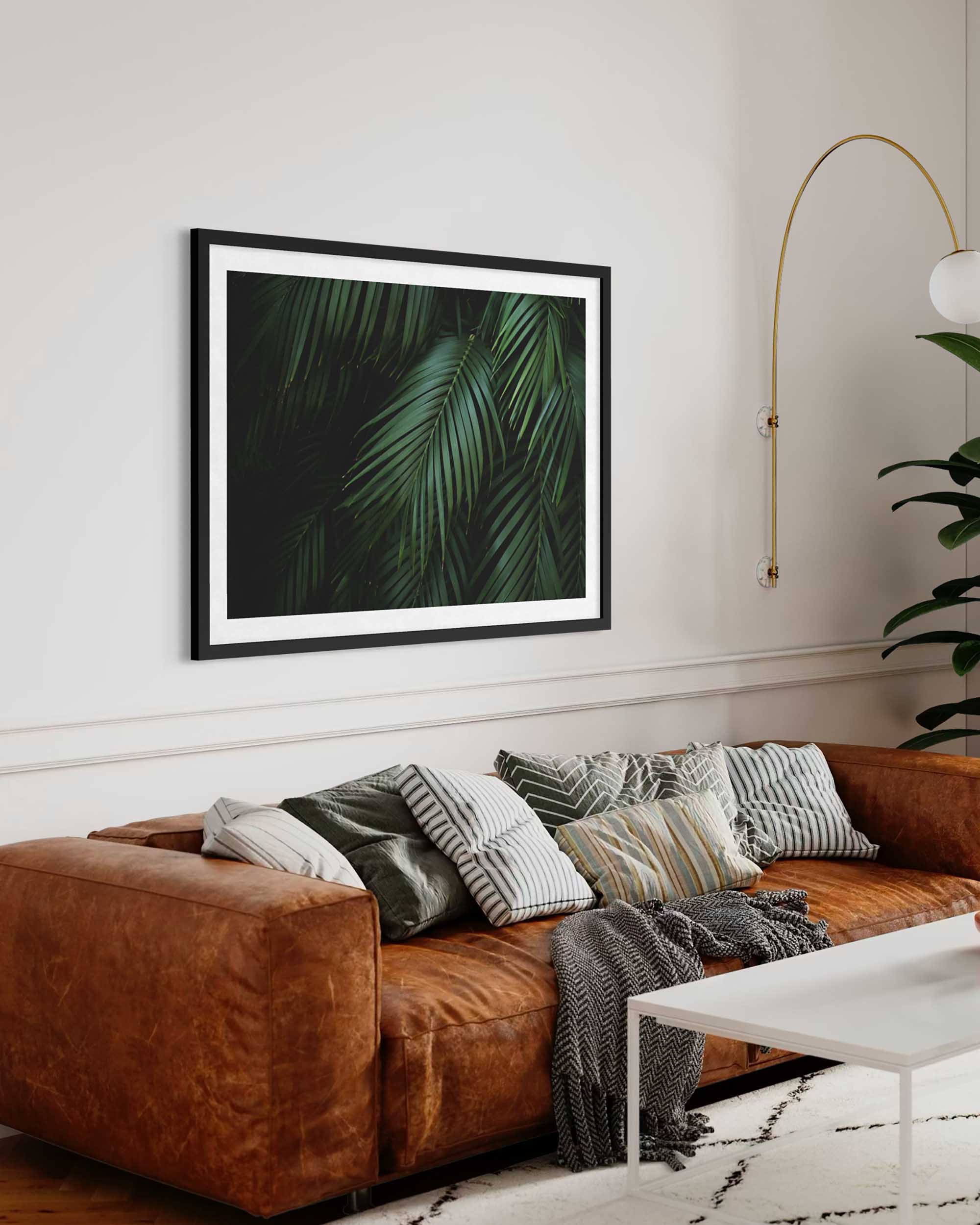 Brown sofa with decorative pillows and a framed leaf print in a living room.