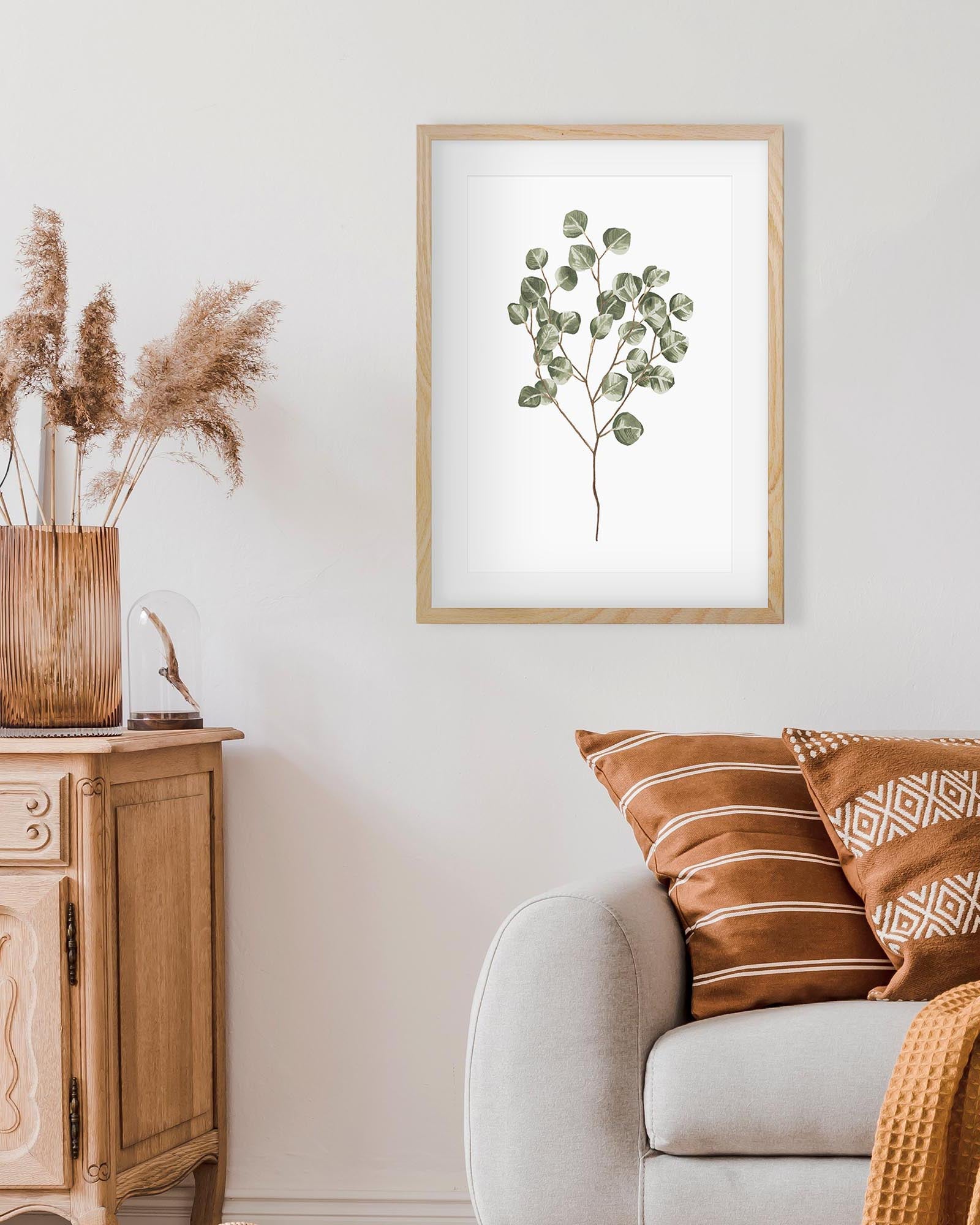 Framed eucalyptus plant art on a wall above a sofa with decorative pillows and a sideboard.