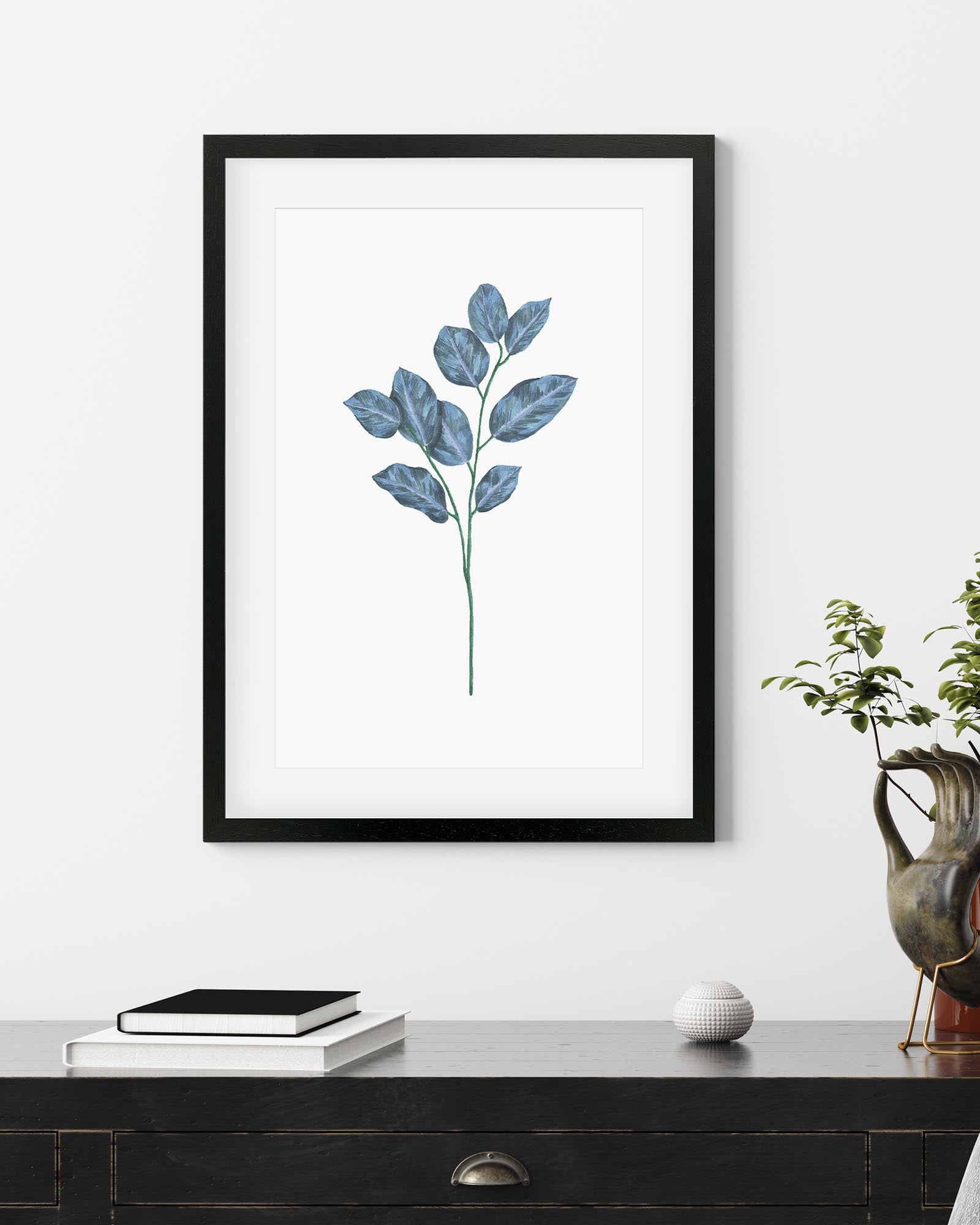 Framed artwork of a leaf design on a white wall above a wooden surface.