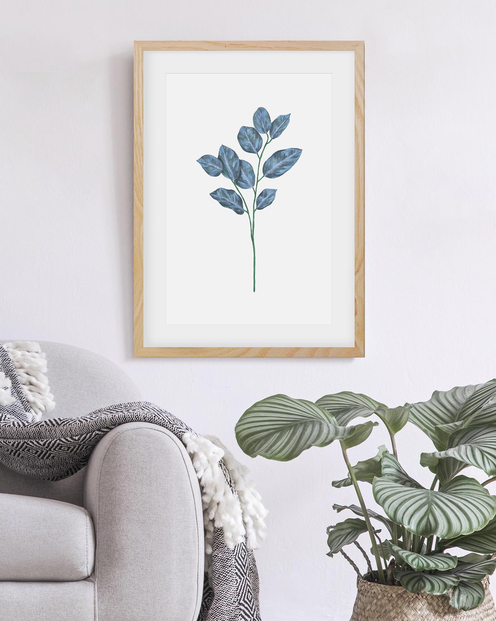 Framed artwork of a leafy plant on a wall above a sofa with a plant in the corner.