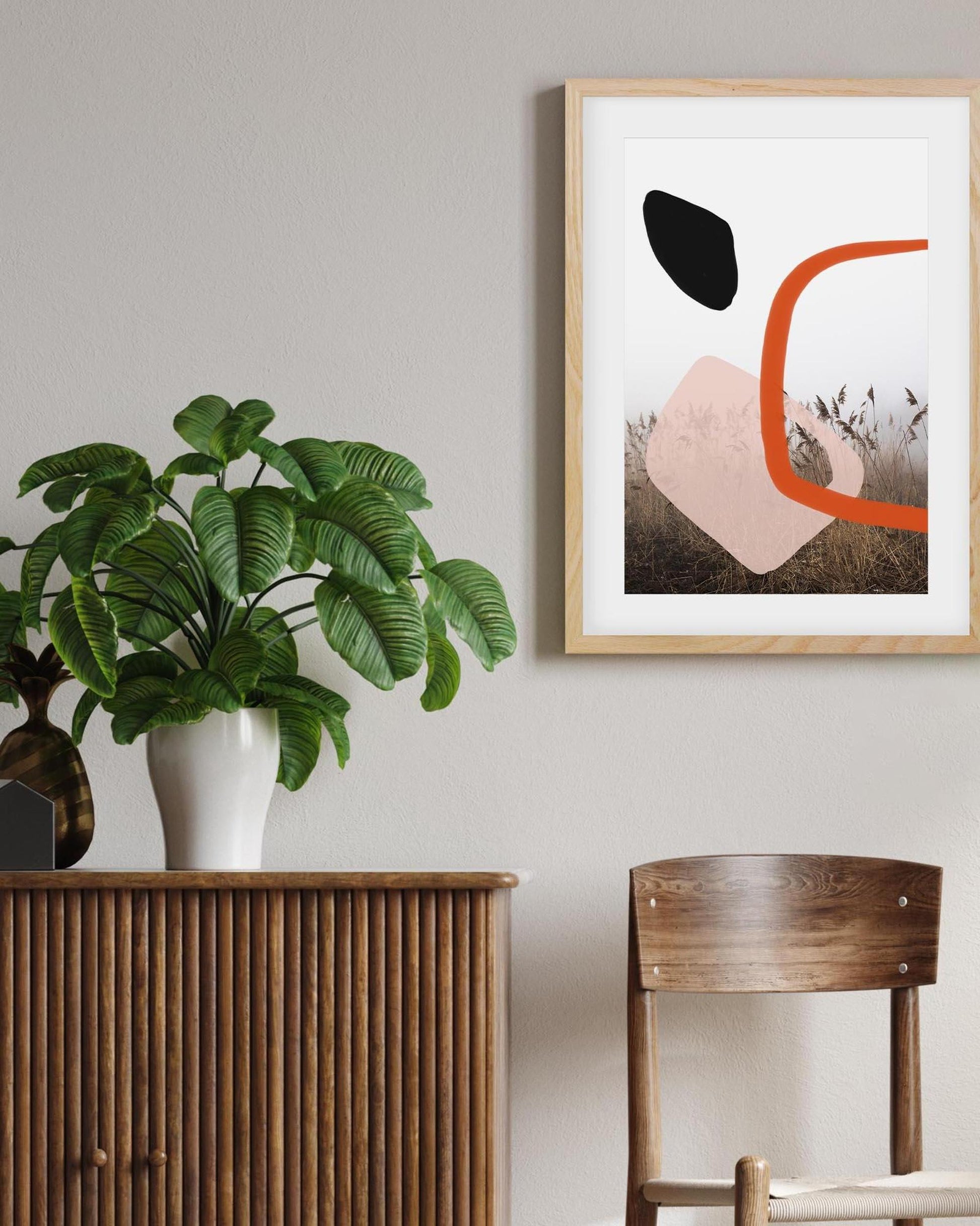 Framed abstract art on a wall with a plant and wooden furniture in the foreground