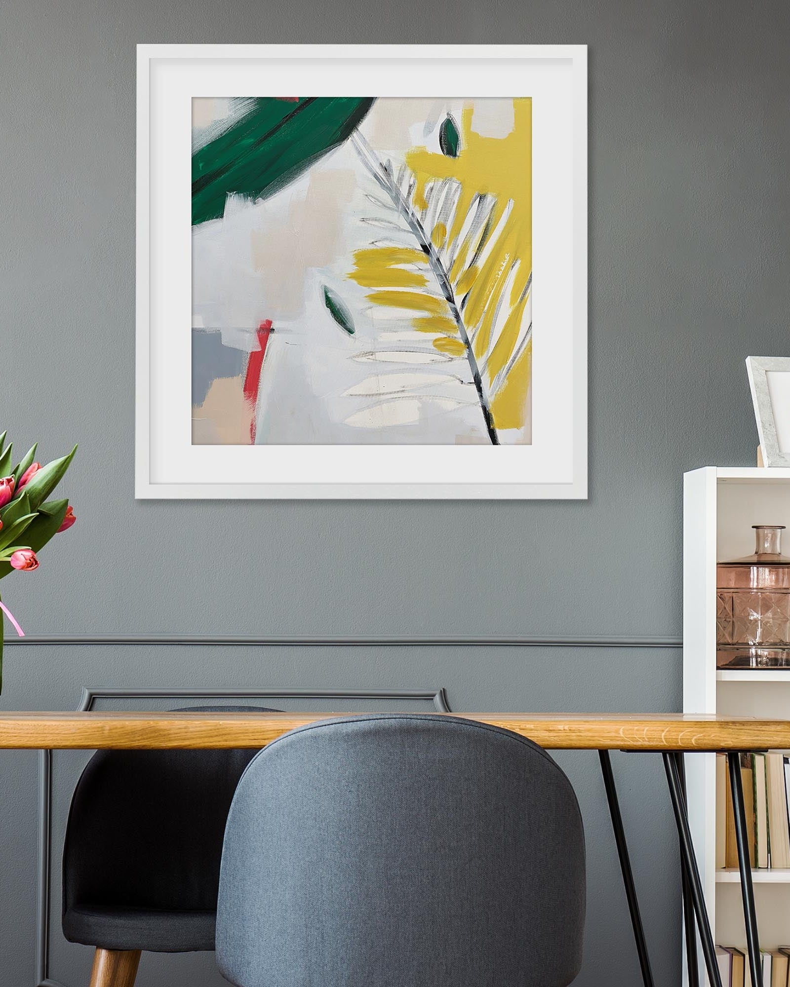 Framed abstract art on a gray wall above a wooden desk with a chair.