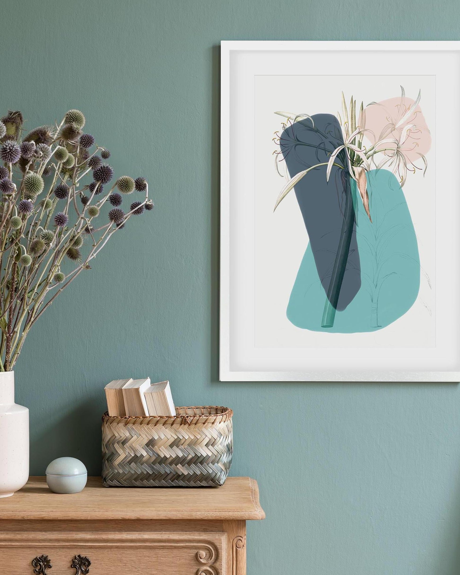 Framed abstract art on a wall with a vase of flowers and basket below.