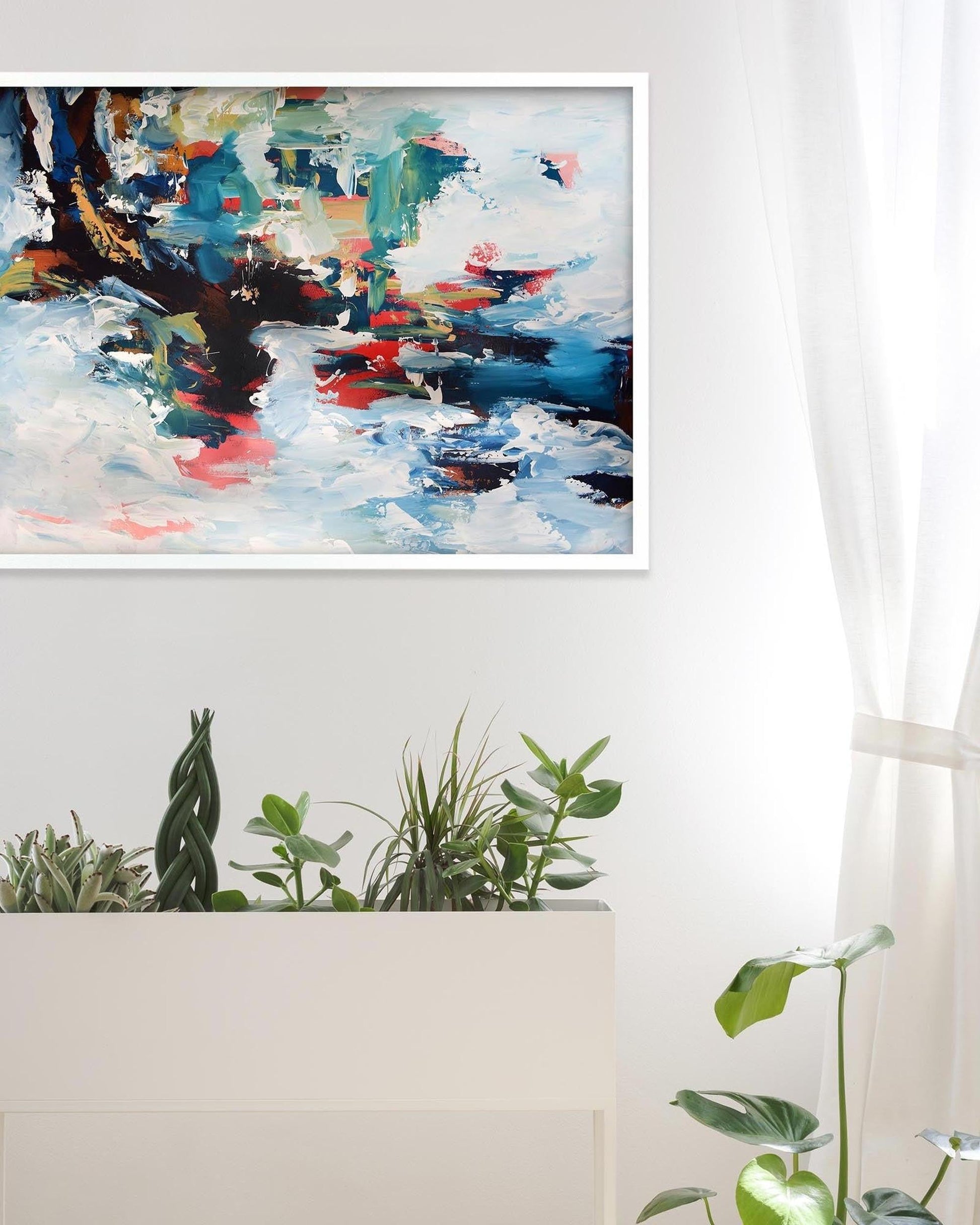 Abstract painting on a wall above a white shelf with plants