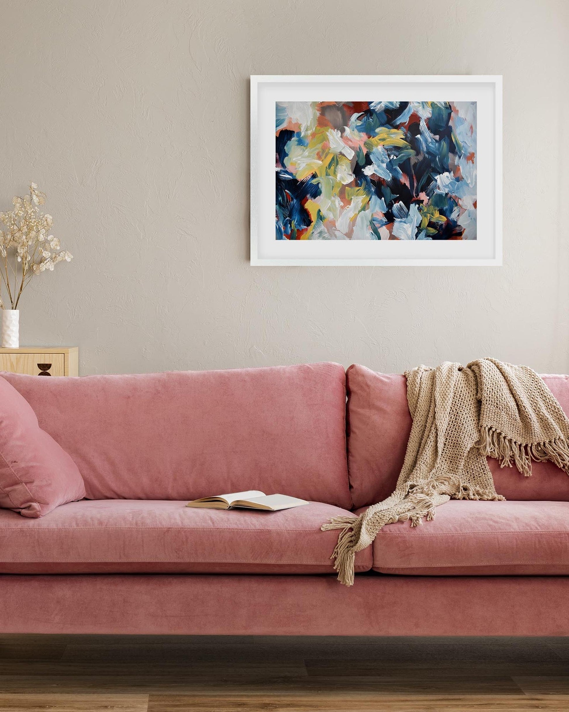 Pink sofa with a blanket and book, framed abstract art on the wall