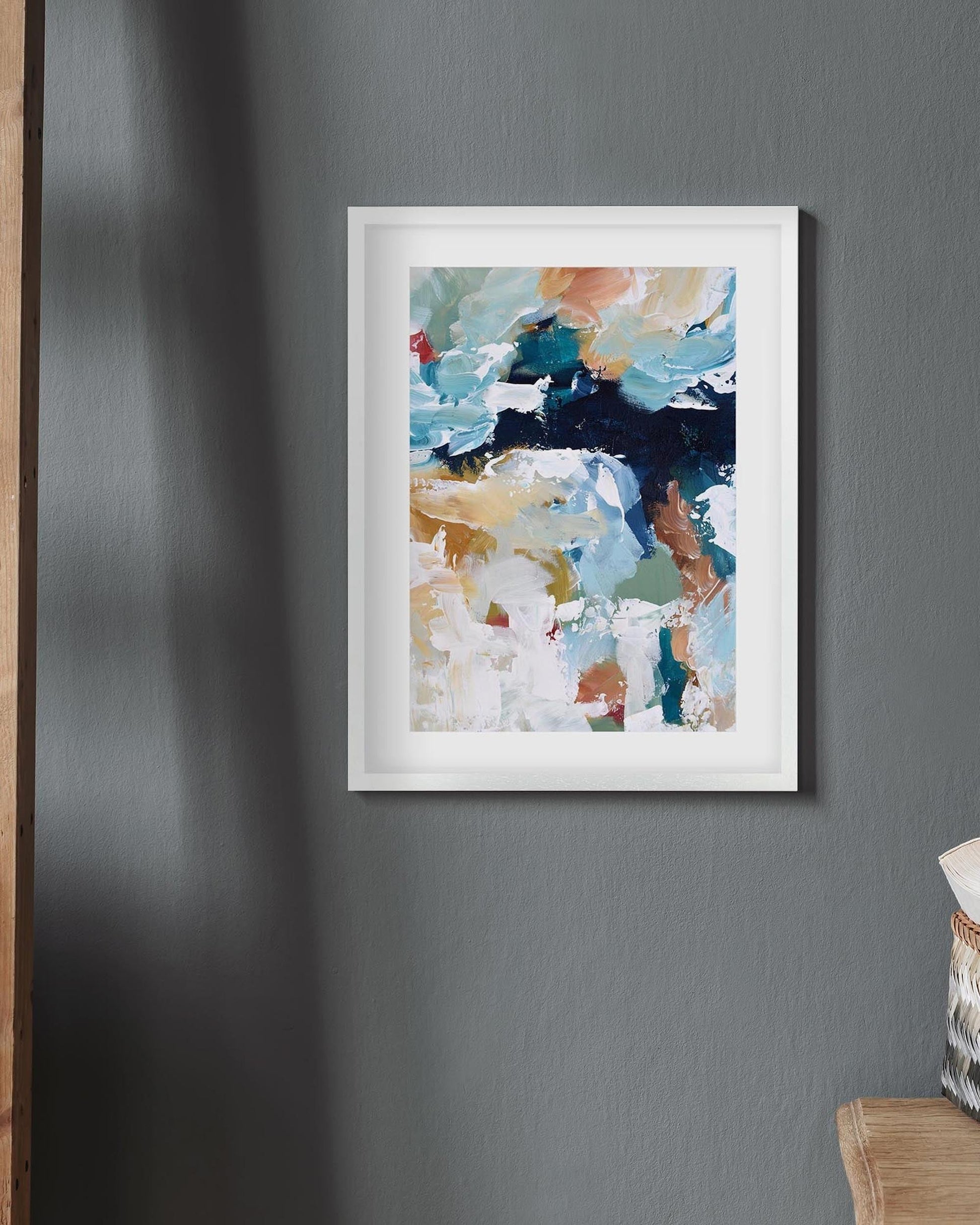 Framed abstract art print on a gray wall with a wooden ladder and basket in the corner.