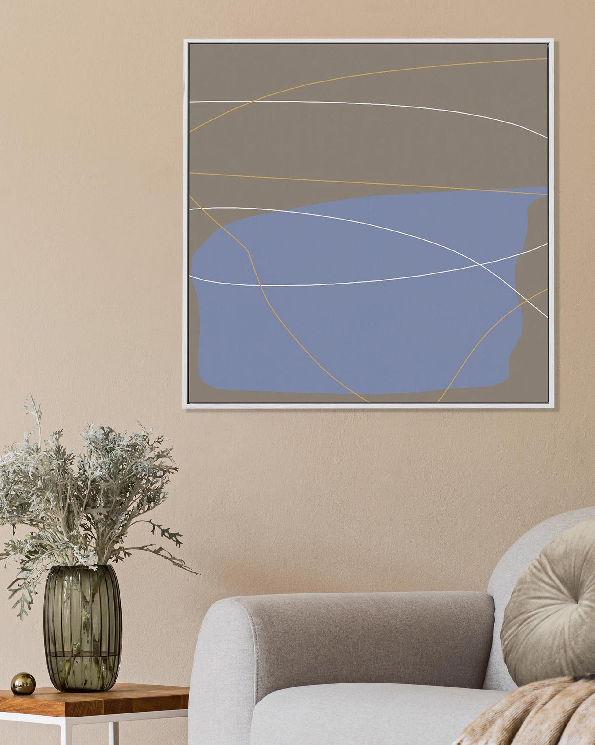 Abstract art piece on a beige wall above a vase with flowers and a chair.