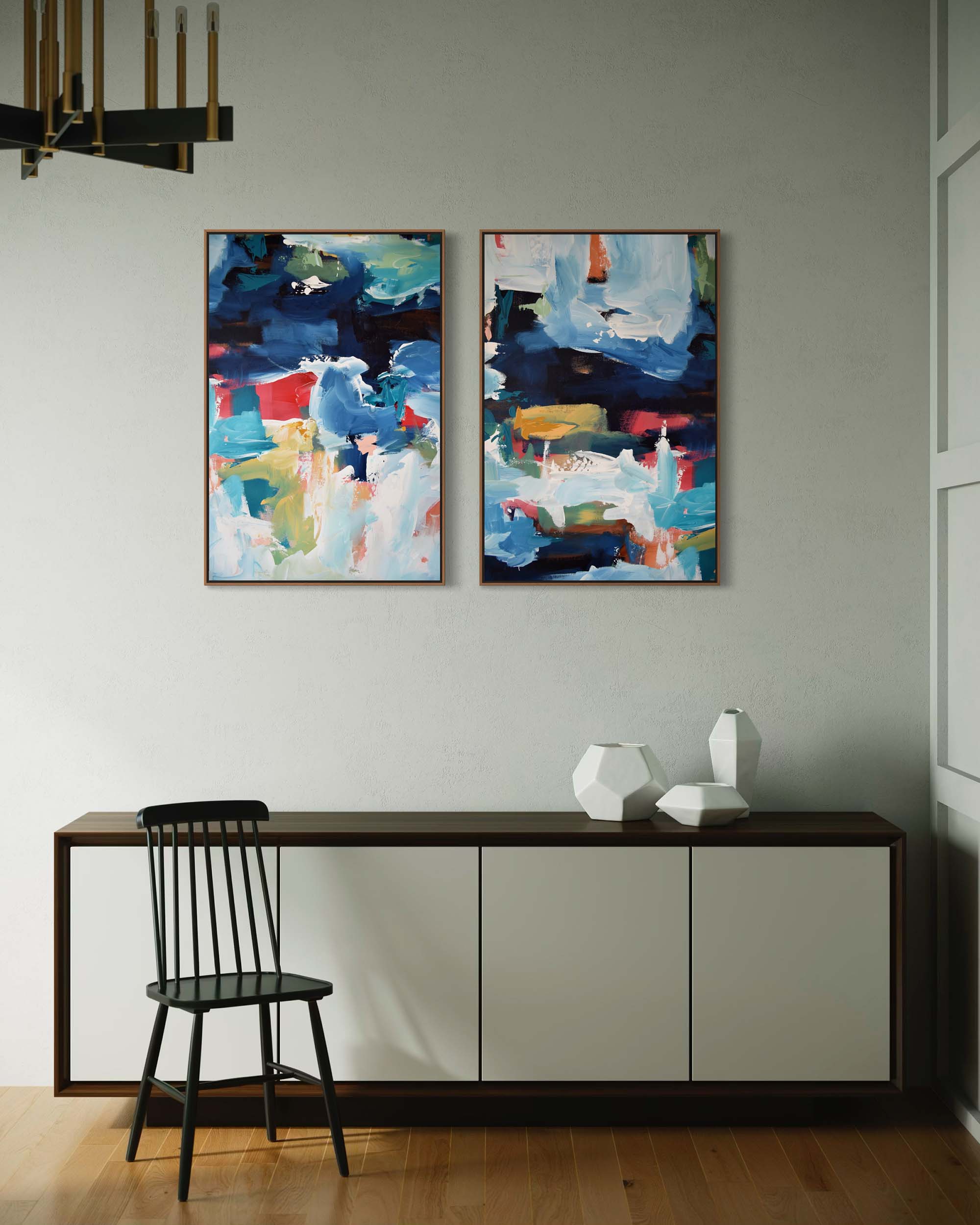 Two abstract paintings on a wall above a console table with a chair and decorative vases.