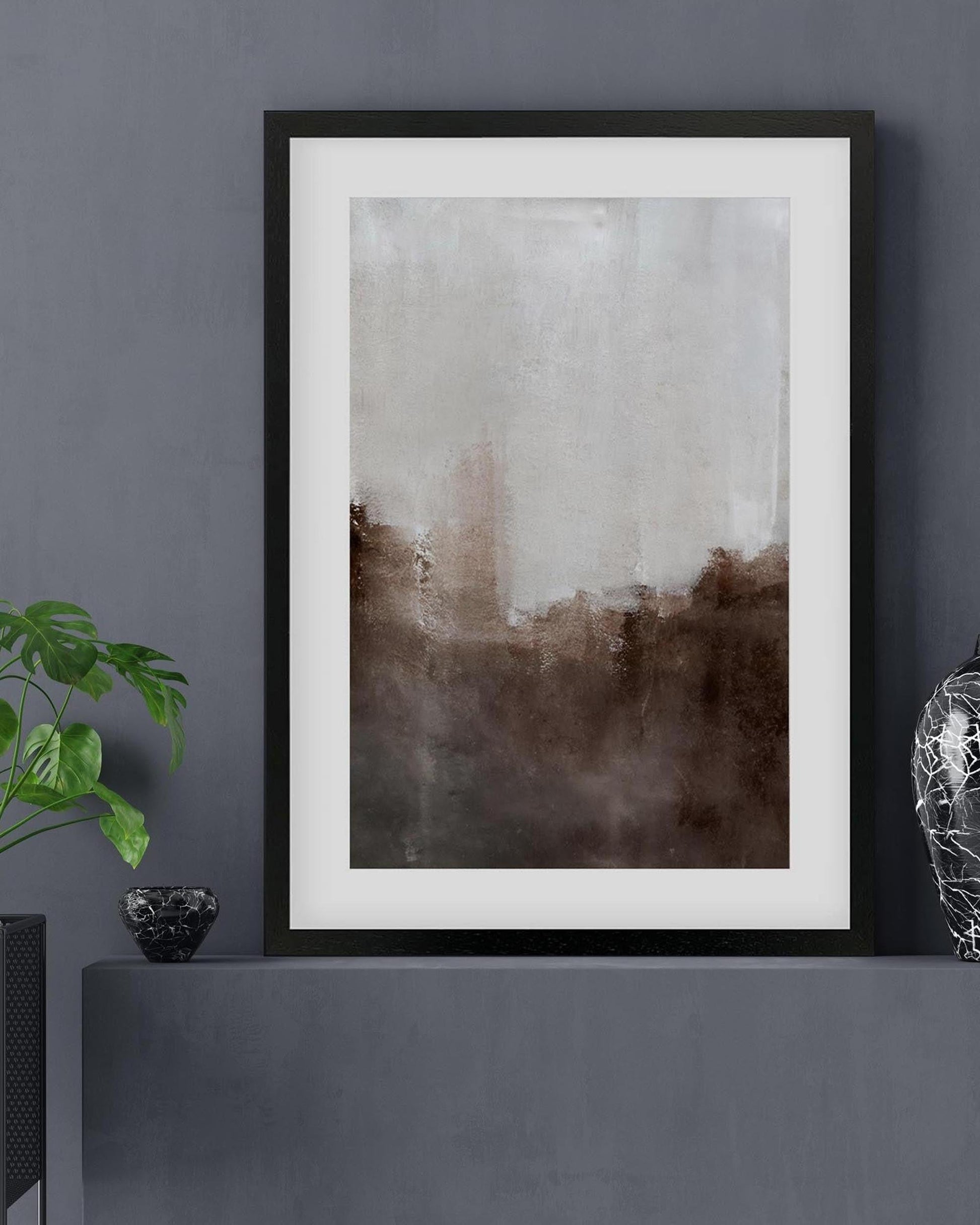 Framed abstract art piece on a gray wall with a plant and decorative object.