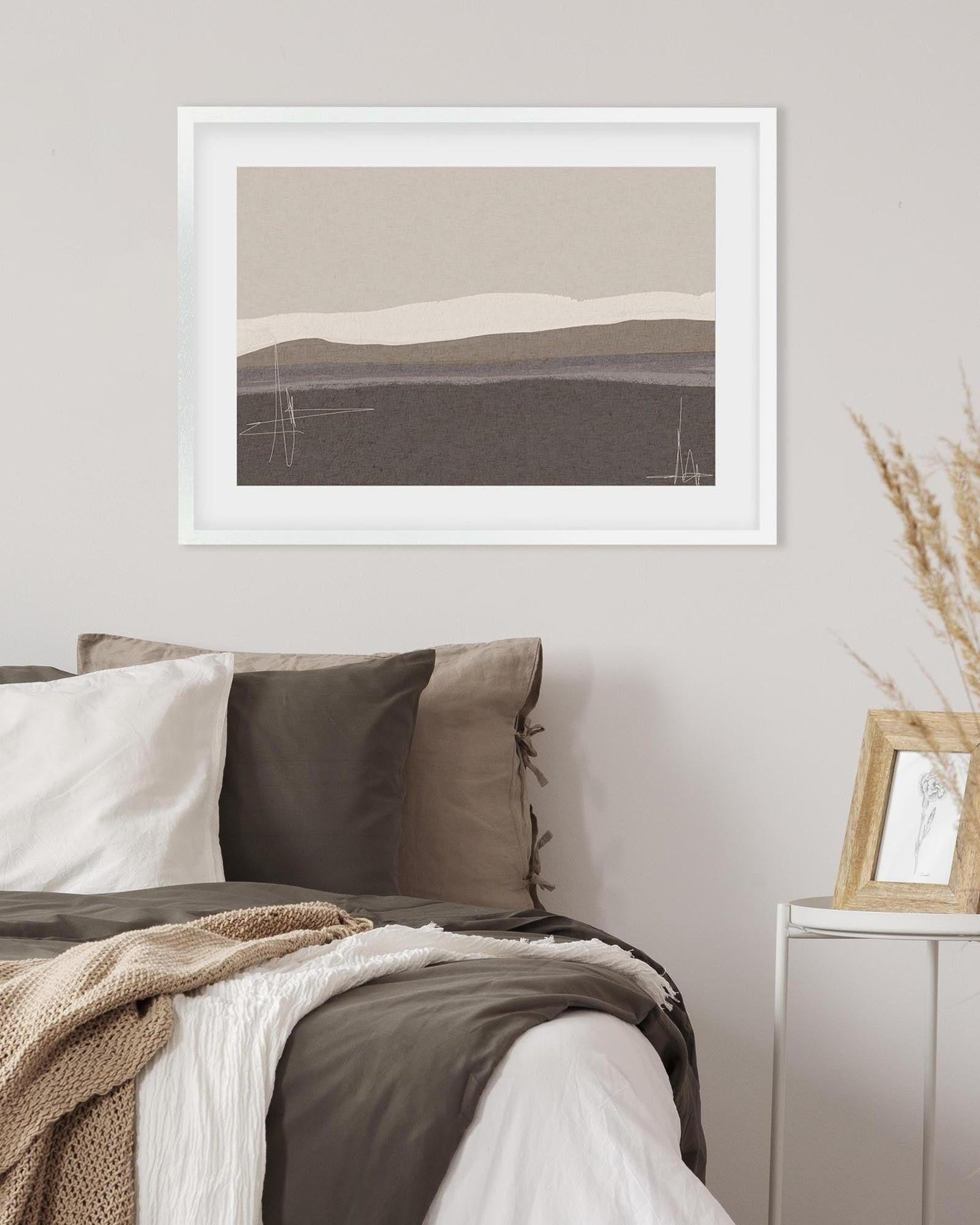 Framed abstract art above a bed with neutral tones