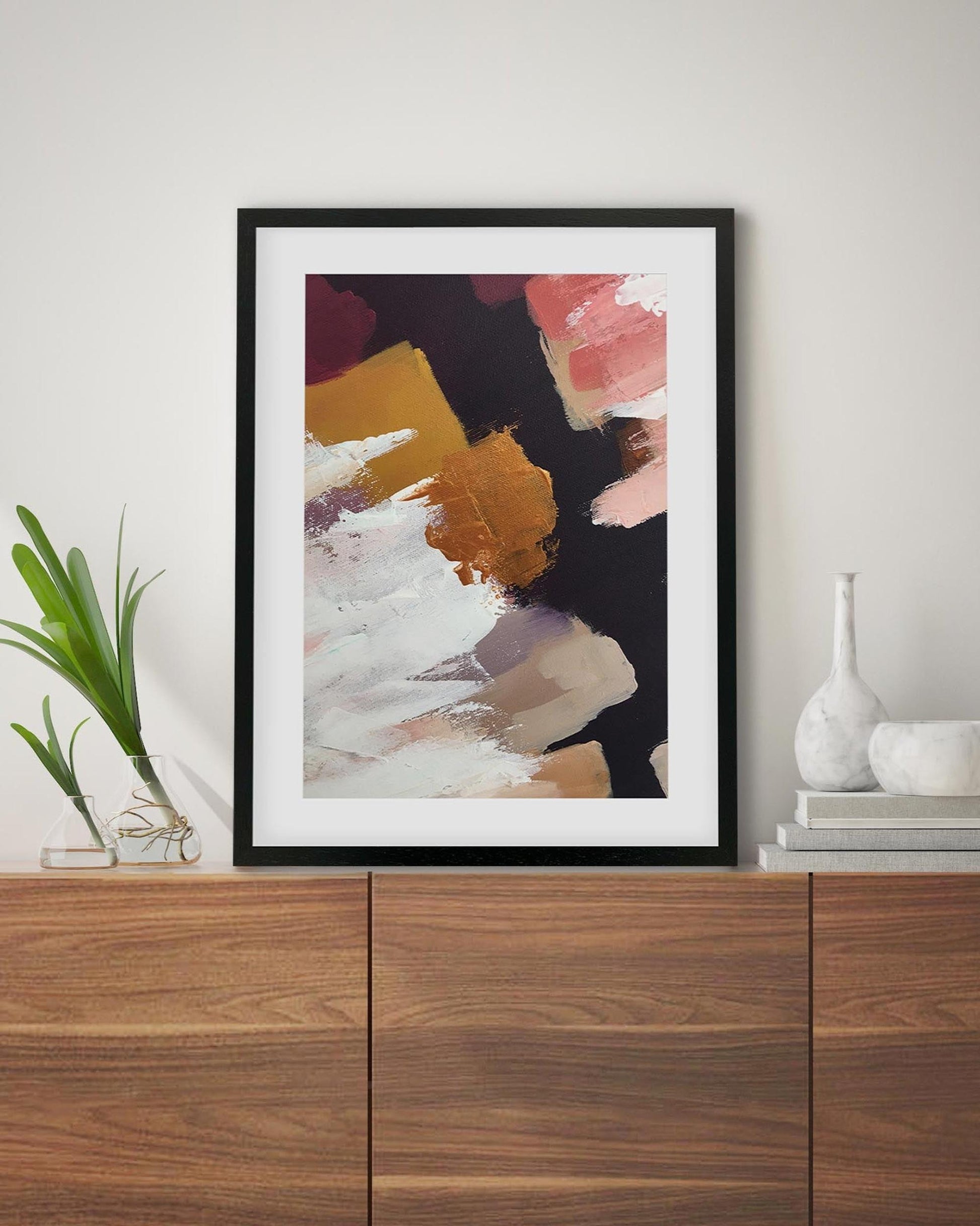 Framed abstract art piece on a wall above a wooden cabinet.