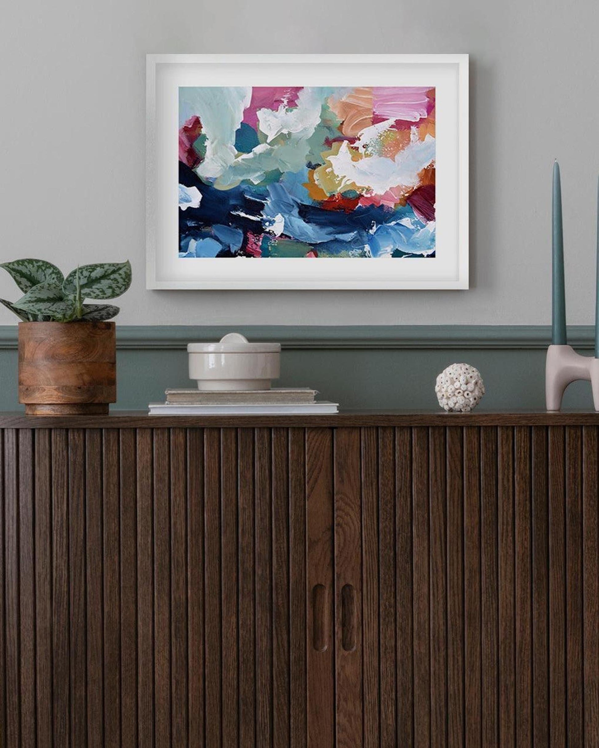 Colorful abstract painting on a wall above a wooden cabinet with decorative items.