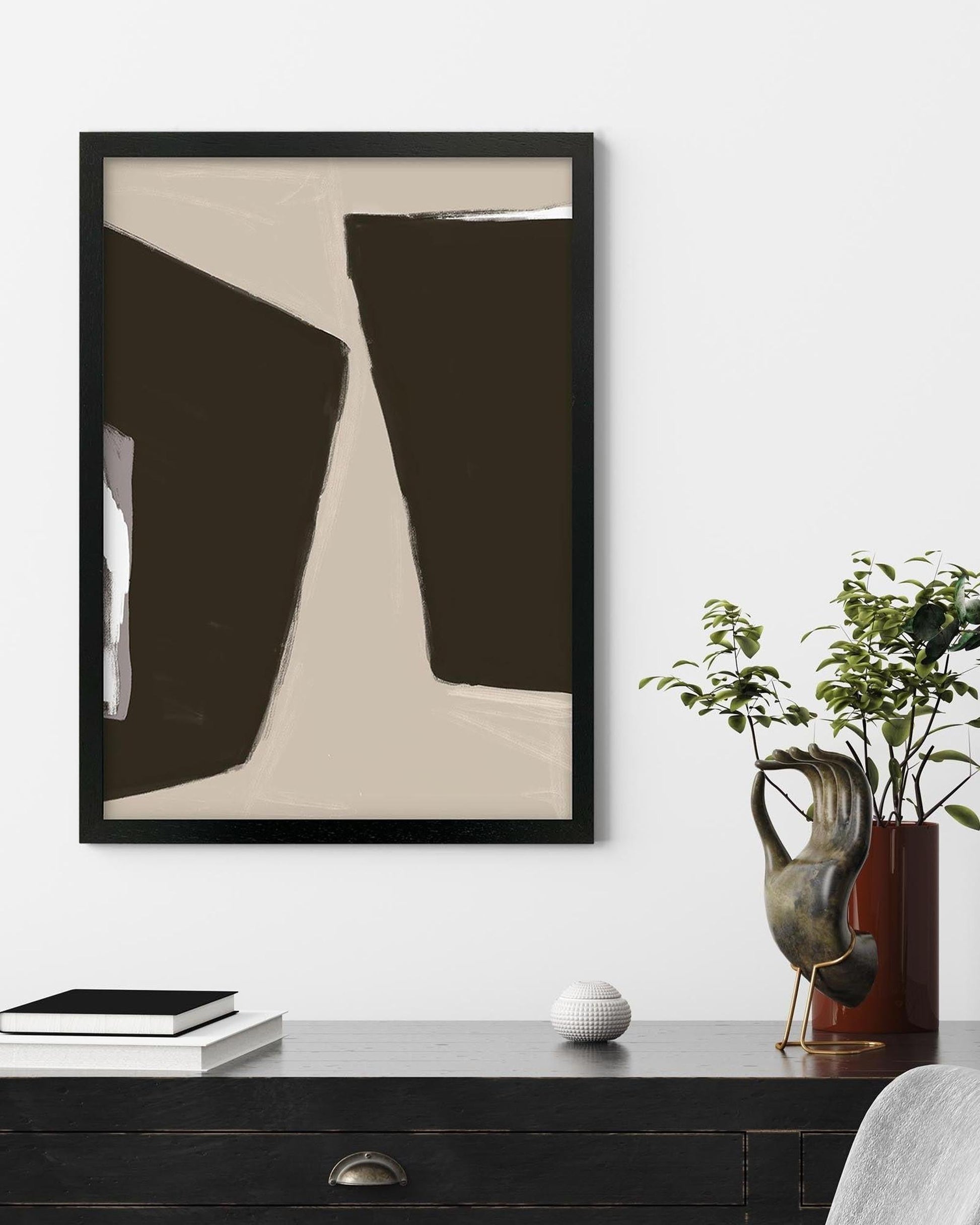 Abstract art piece in a black frame on a wall above a dark wooden desk with decorative items.