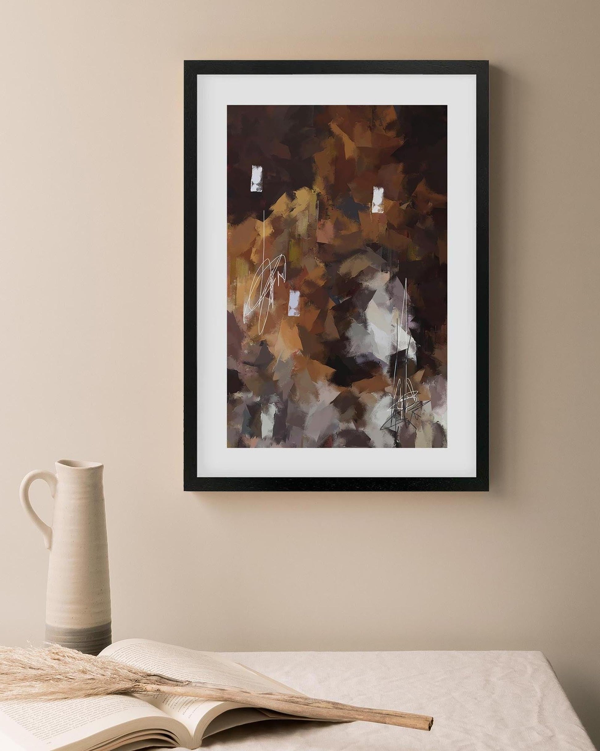 Framed abstract art piece on a beige wall with a vase and book in the foreground.