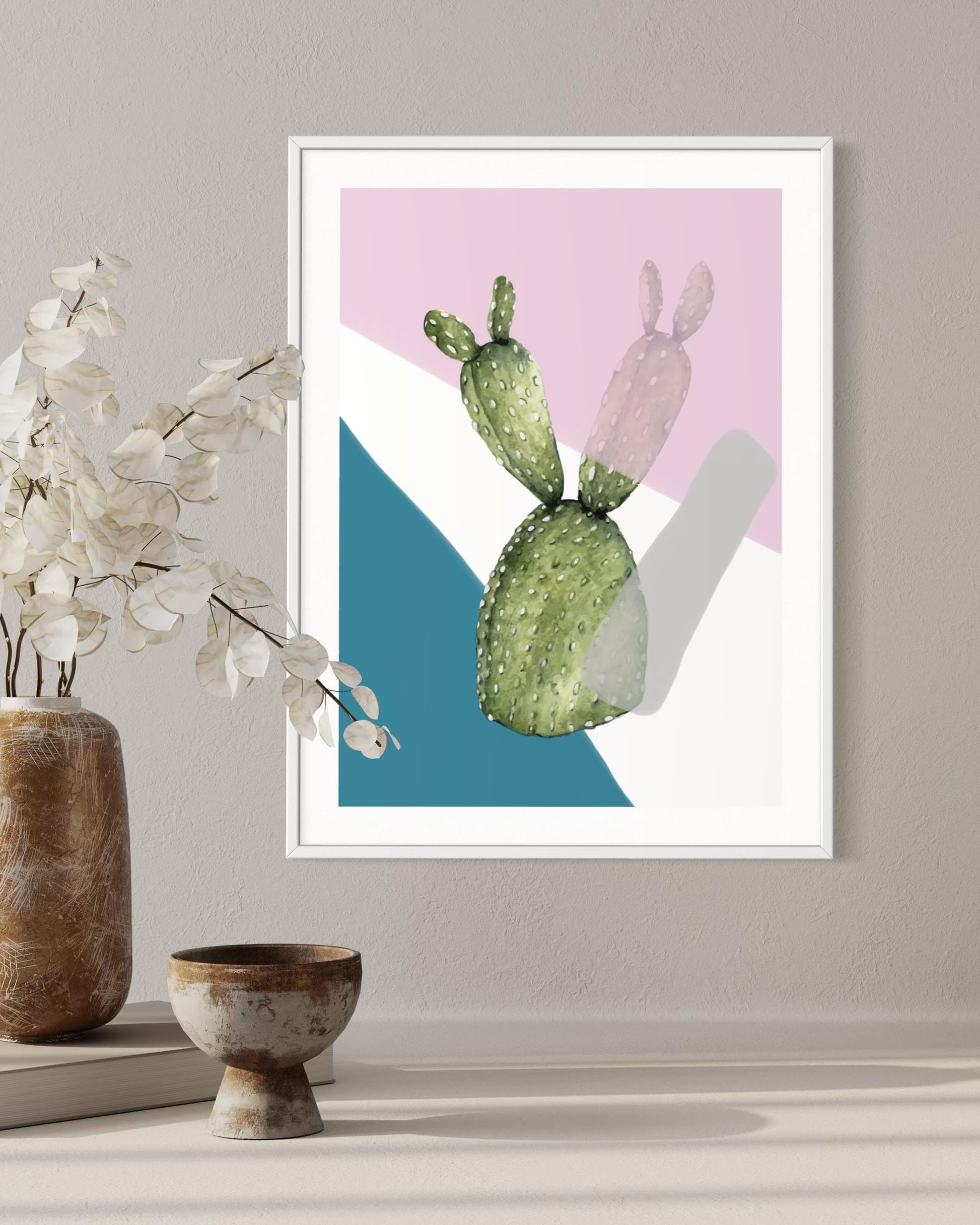 Framed artwork of a cactus with abstract geometric shapes on a wall with decorative items below.